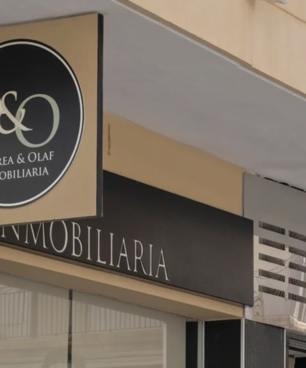 Buitenzijde van het kantoor van Andrea & Olaf Inmobiliaria, met een rond logo op een gevel van zwarte natuursteen en een glazen pui.