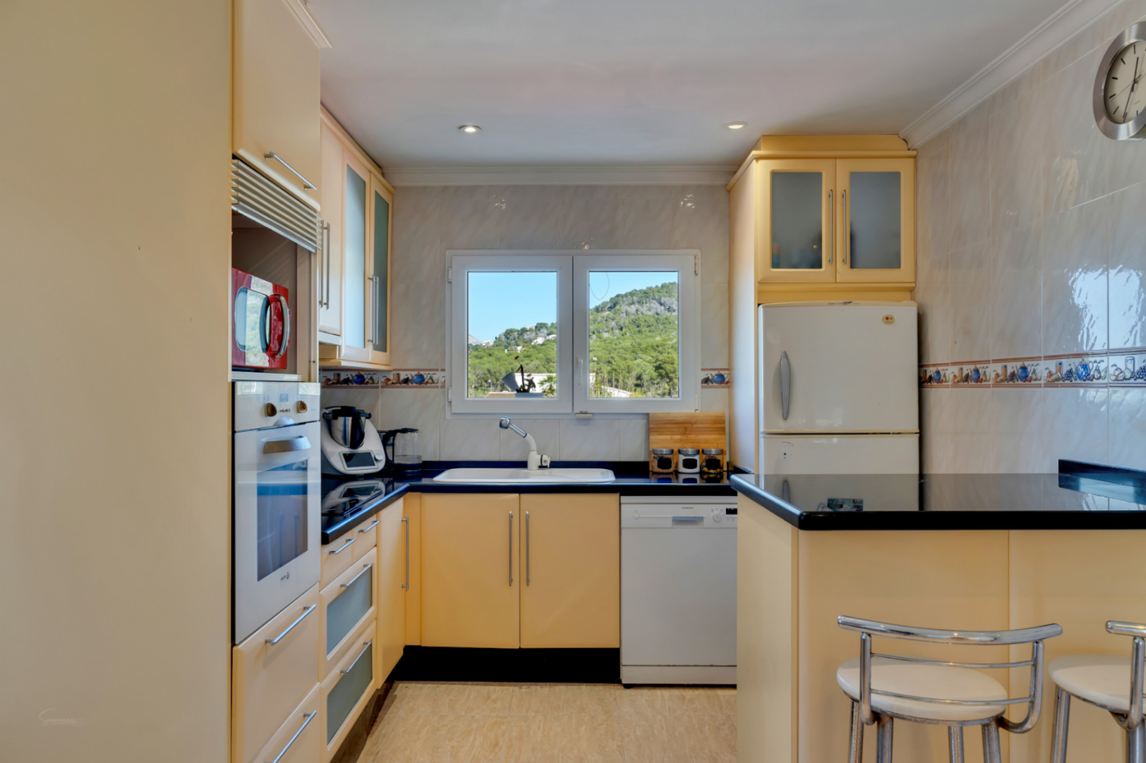 Functionele keuken met crèmekleurige kasten, zwart granieten werkbladen en een raam met uitzicht op de bergen. Voorzien van inbouwapparatuur en een ontbijtbar.