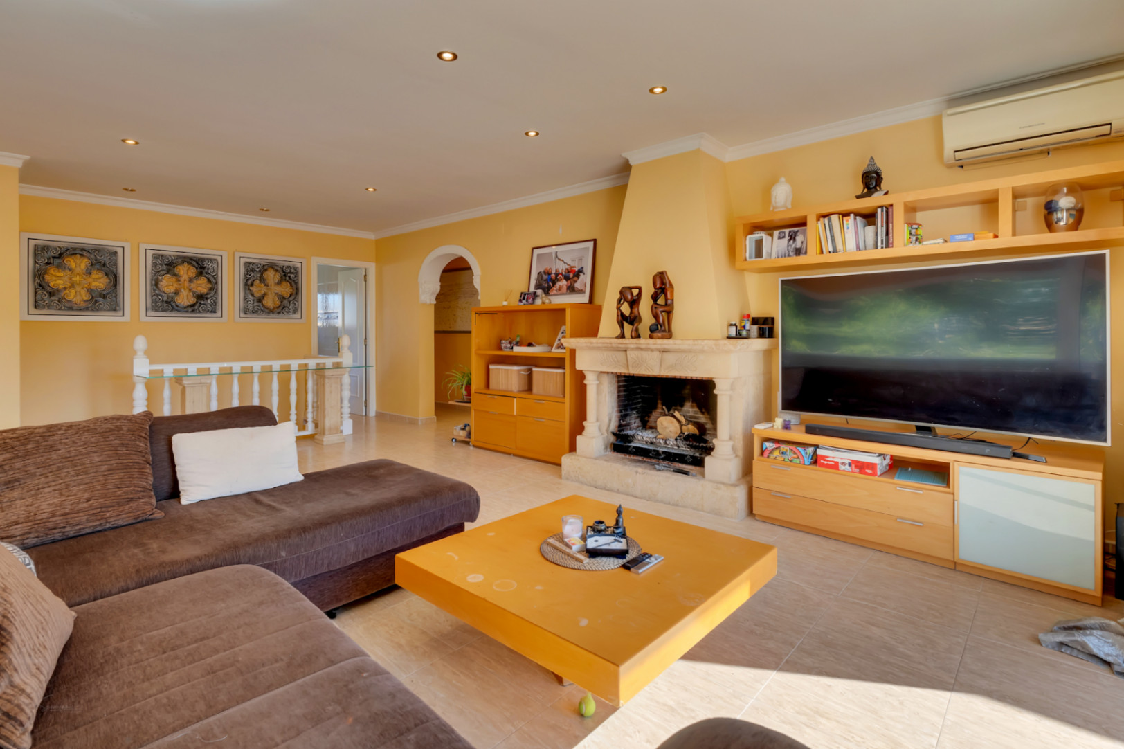 Lichte woonkamer met een natuurstenen schouw, houten maatwerkmeubels en een ruime zithoek voorzien van een tegelvloer.