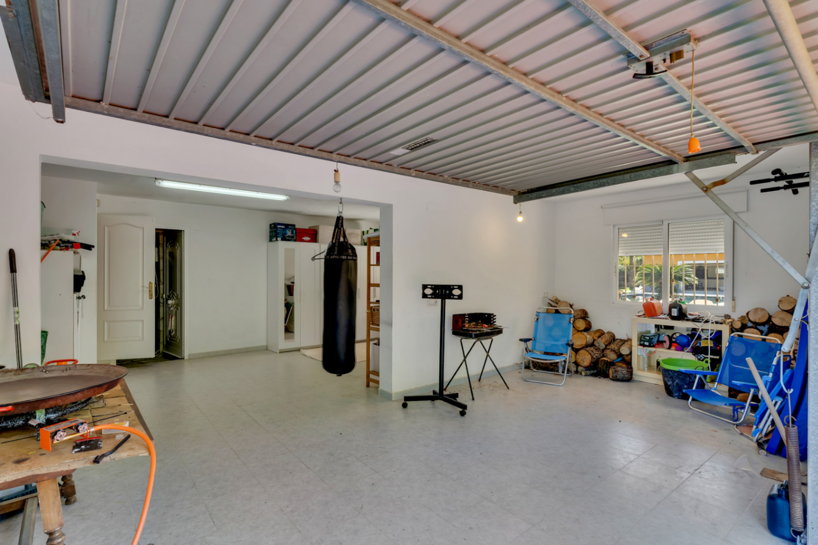 Ruime multifunctionele garage met metalen plafond en tegelvloer. Veelzijdige ruimte geschikt voor opslag, fitness en brandhout met directe toegang tot de woning.