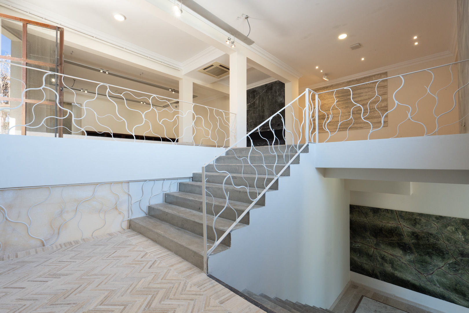 Architecturale trap met een wit organisch gevormd hekwerk, die de commerciële verdiepingen verbindt, voorzien van visgraatvloeren en decoratieve stenen wandpanelen.