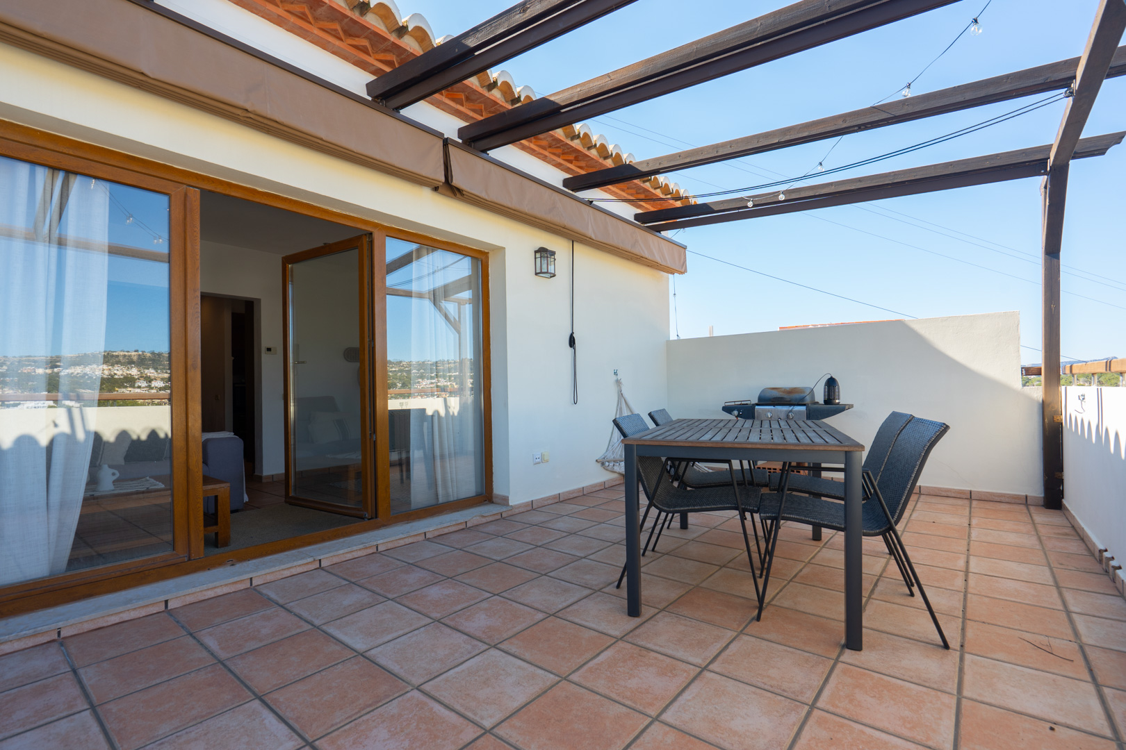 Bovenste terras met terracotta tegels, een houten pergola en een eethoek buiten. Grote glazen schuifdeuren verbinden de buitenruimte met het woongedeelte.