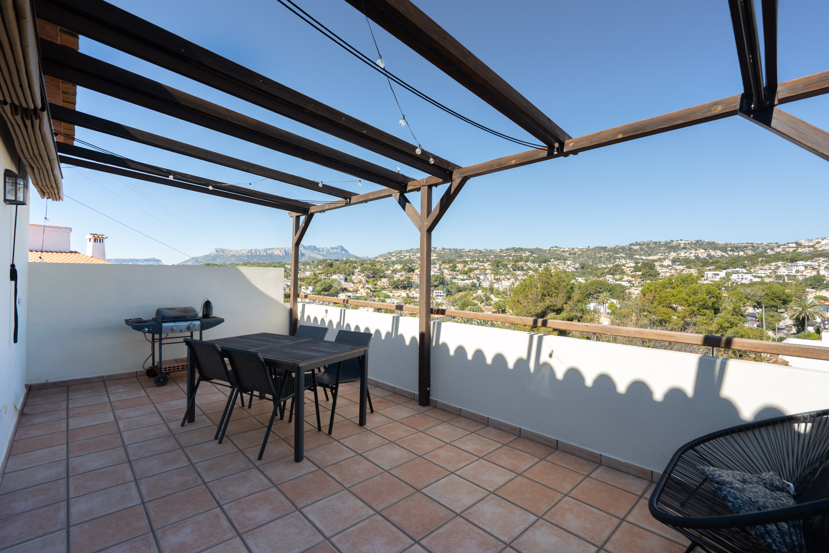 Bovenste terras met terracotta tegels, een houten pergola en eethoek. Het biedt een panoramisch uitzicht op de Sierra de Bernia en de omliggende vallei.