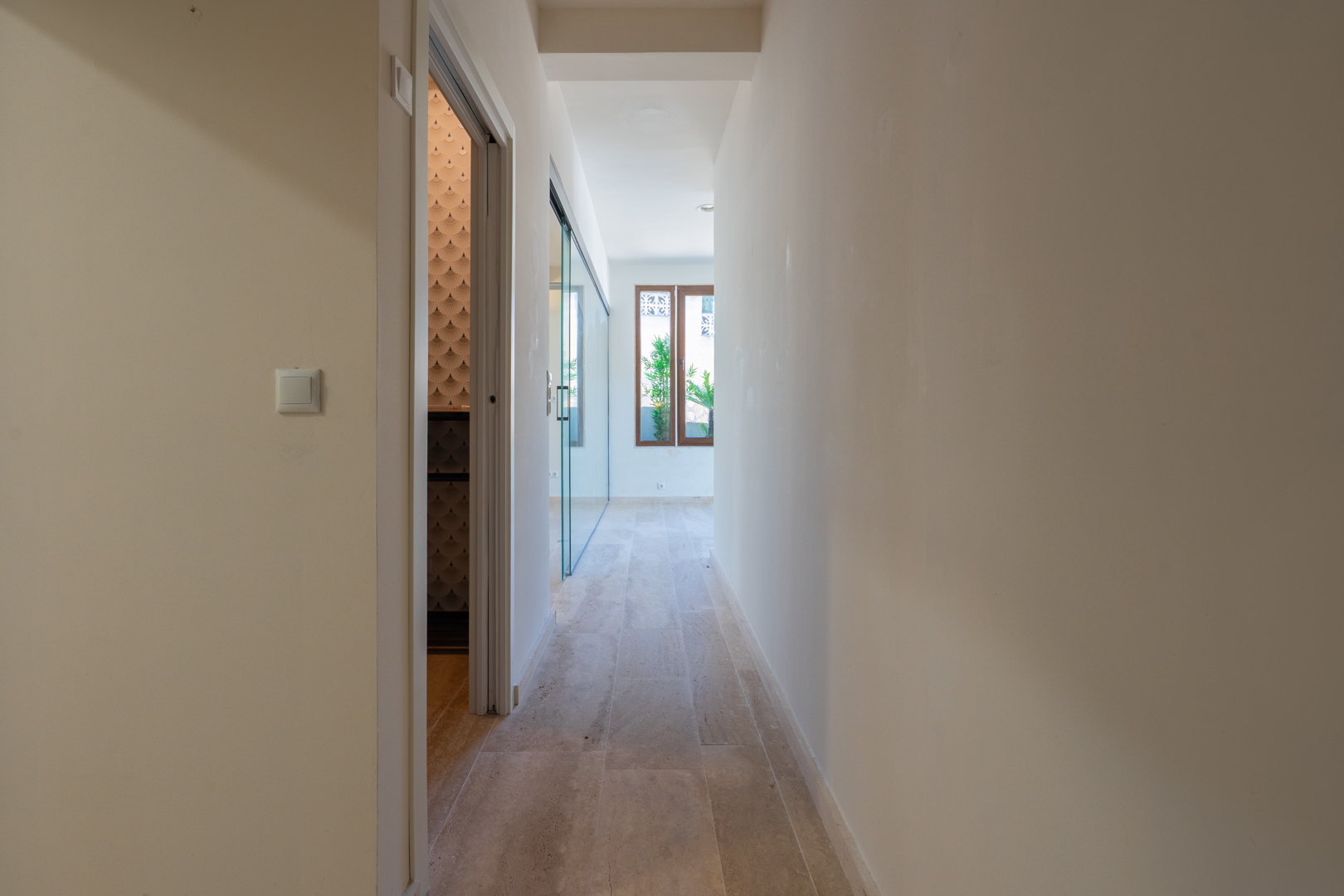 Distributiegang met stenen vloer, neutrale wanden en toegang tot kamers met designbehang en glazen scheidingswanden.