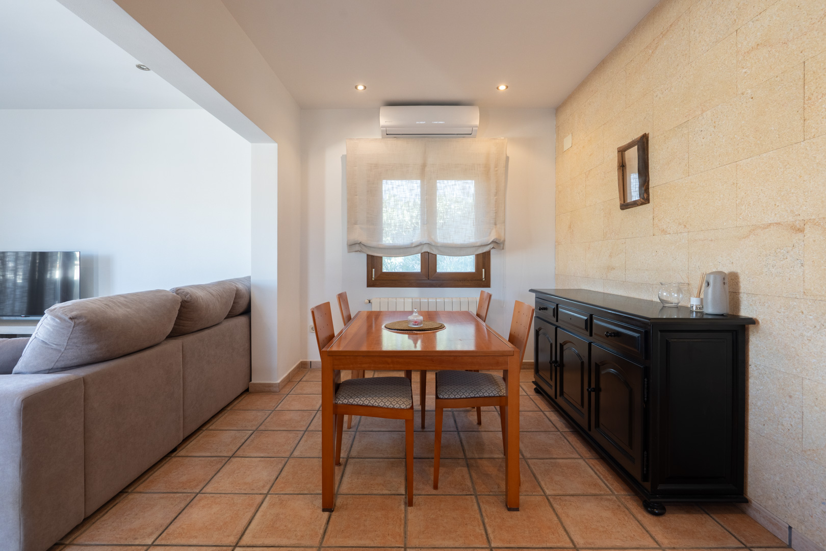 Eethoek met houten tafel, zwart dressoir en natuurstenen wand. Voorzien van terracotta vloertegels, airconditioning en subtiele inbouwspots.