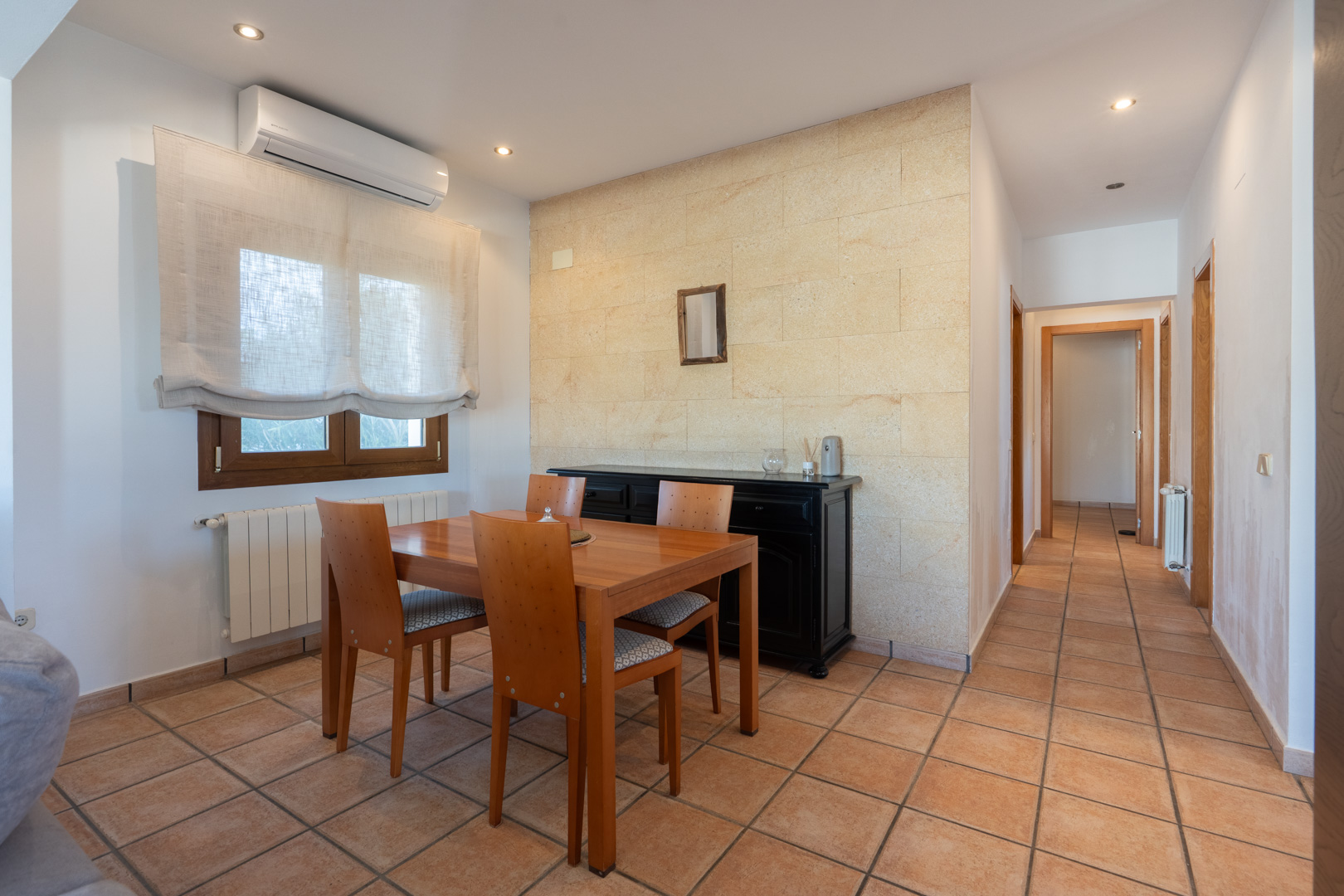 Eethoek van de woning met natuurstenen accentmuur, terracotta vloer, airconditioning en een gang die naar de slaapkamers leidt.