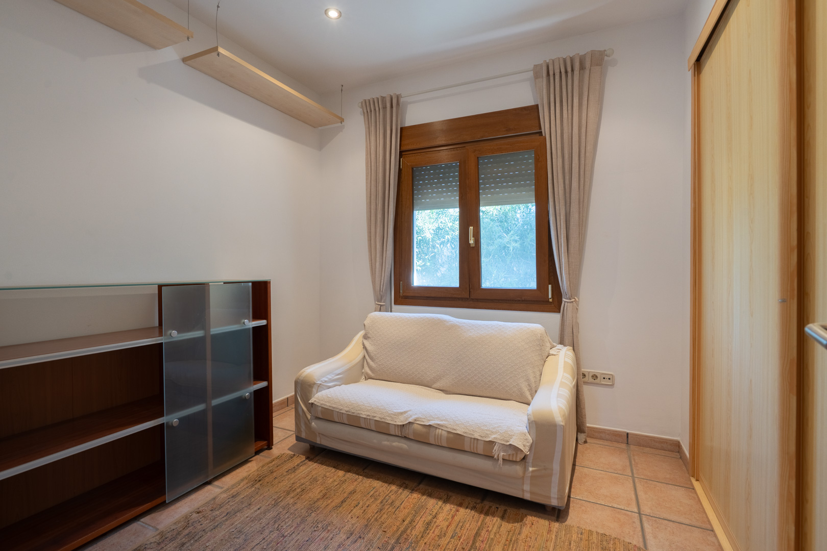 Functionele kamer met terracotta tegels, houten raam met rolluiken en inbouwkast. Voorzien van wandplanken, inbouwspots en een kleine zitbank.