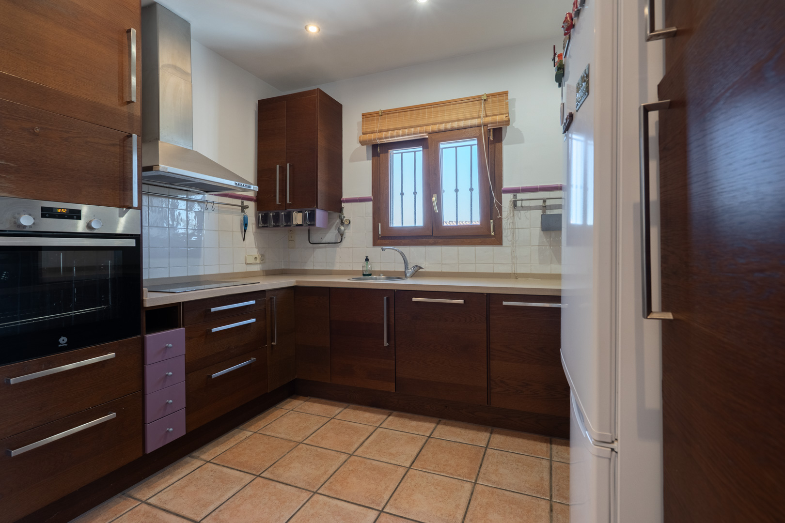 Functionele keuken met donkerhouten kasten, inbouwoven van Balay en een tegelvloer. Voorzien van een roestvrijstalen afzuigkap en een raam met houten kozijn.