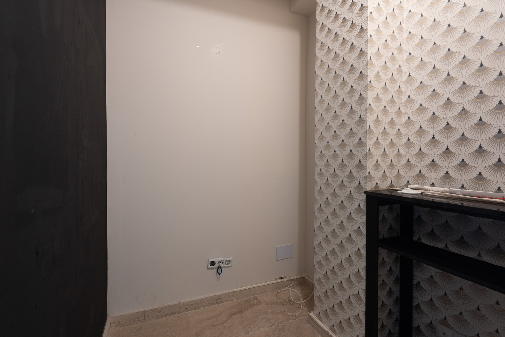 Interieurhoek met geometrisch behang, neutrale witte wanden voorzien van stopcontacten en een lichte natuurstenen vloer.