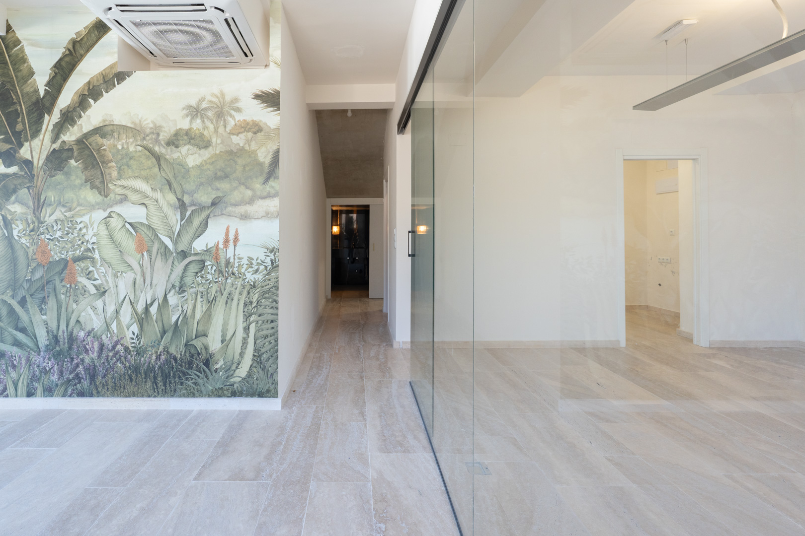Lichte commerciële ruimte met een natuurstenen vloerlook, glazen scheidingswand en botanisch behang. Voorzien van een airconditioning aan het plafond.