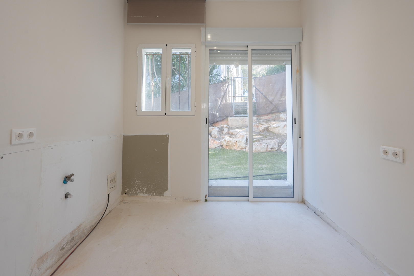 Lichte ruimte met aansluitingen voor sanitair, witte aluminium kozijnen en een glazen schuifdeur die toegang biedt tot de tuin.