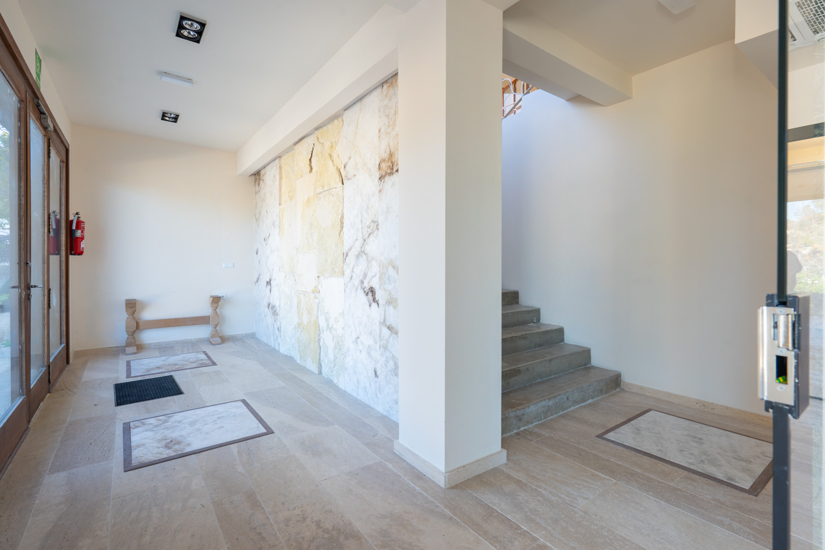 Ontvangsthal met een decoratieve natuurstenen wand, tegelvloer met marmeren inlays en trap naar de bovenverdiepingen.