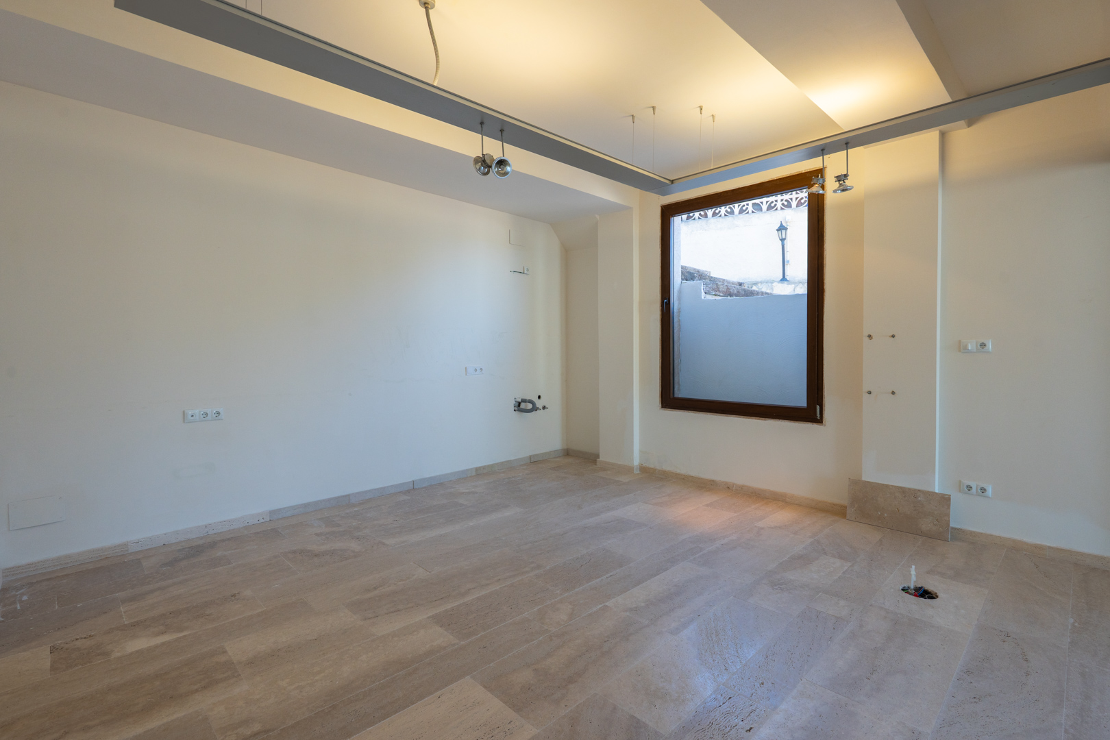 Open binnenruimte met natuurstenen vloer, inbouwverlichting en een groot raam met houten kozijn. Voorzien van aansluitingen voor elektra en sanitair aan de wanden.