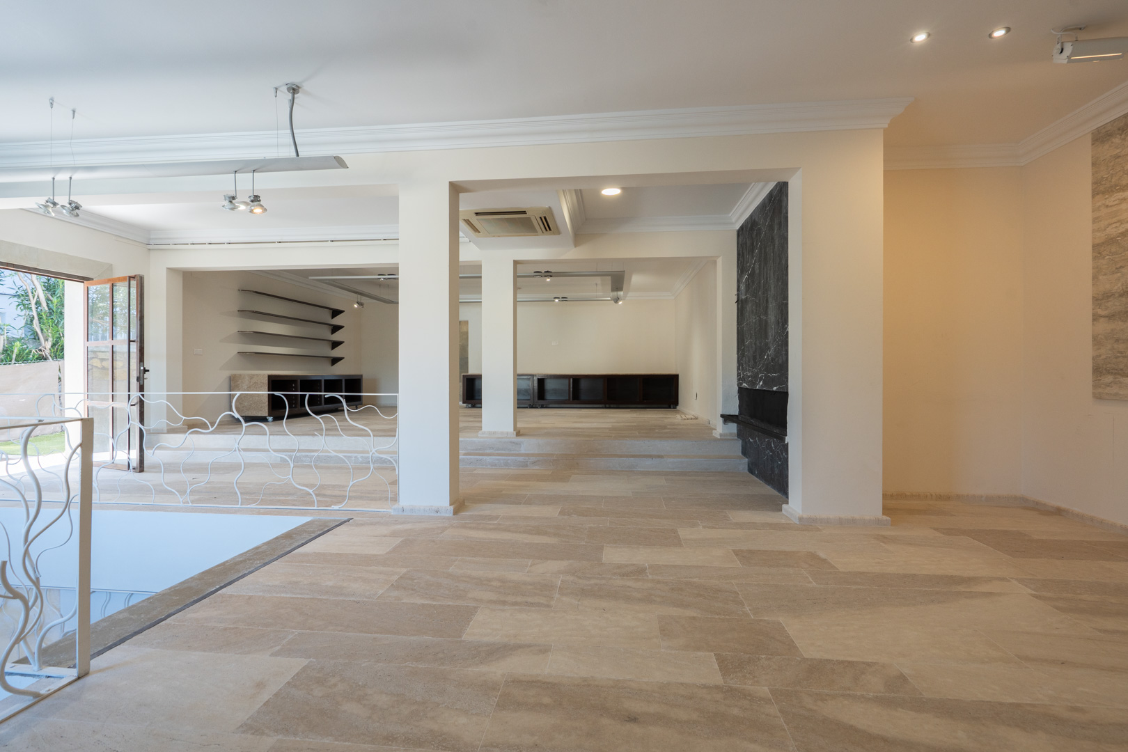 Ruime open verdieping met natuurstenen vloer, structurele kolommen, inbouwspots en een accentmuur van zwart marmer.