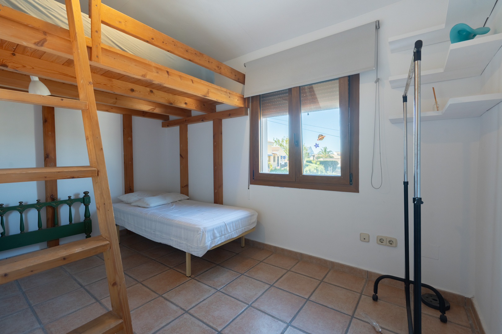 Slaapkamer met een massief houten stapelbed, rustieke tegelvloer en een raam met houten kozijn voor natuurlijk lichtinval.