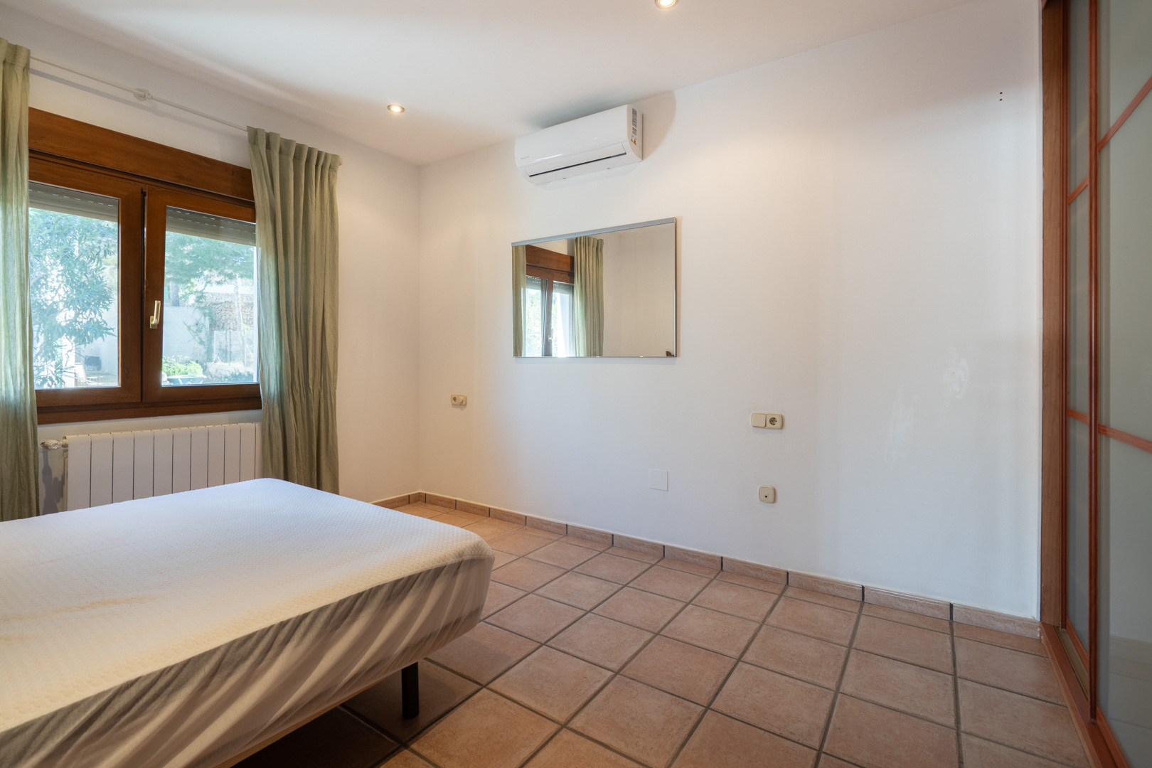 Slaapkamer met tegelvloer, split-airconditioning, houten raamkozijn en een inbouwkast met doorschijnende schuifdeuren.