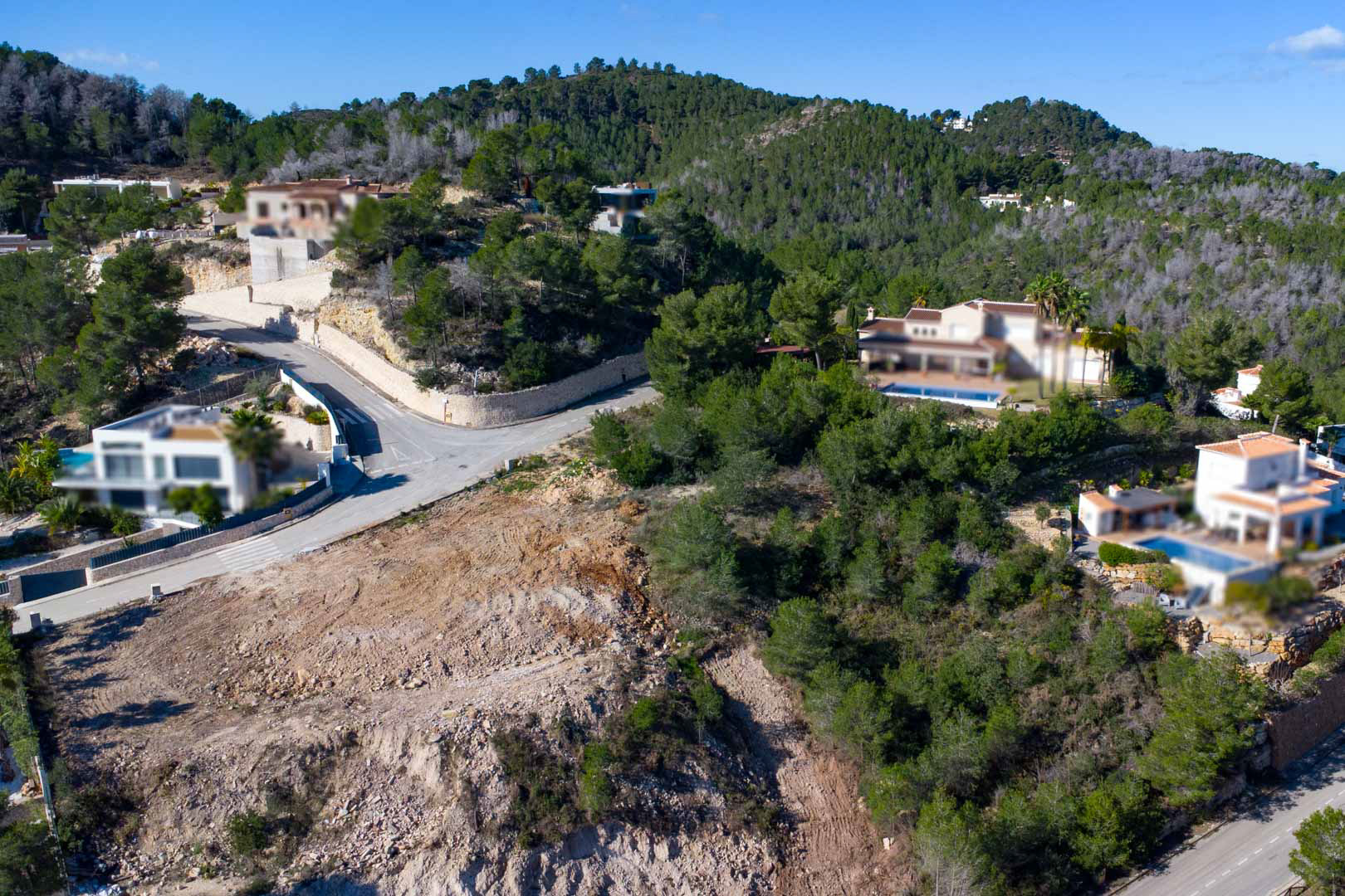 Luchtfoto van het verhoogde perceel omgeven door dennenbossen, met de voorbereide bouwplaats en naburige villa's met privézwembaden.