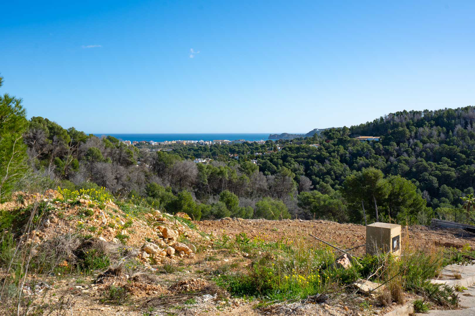 Panoramisch uitzicht op de zee en de kust vanaf het hoger gelegen perceel, omringd door een dicht mediterraan dennenbos en een natuurlijk landschap.