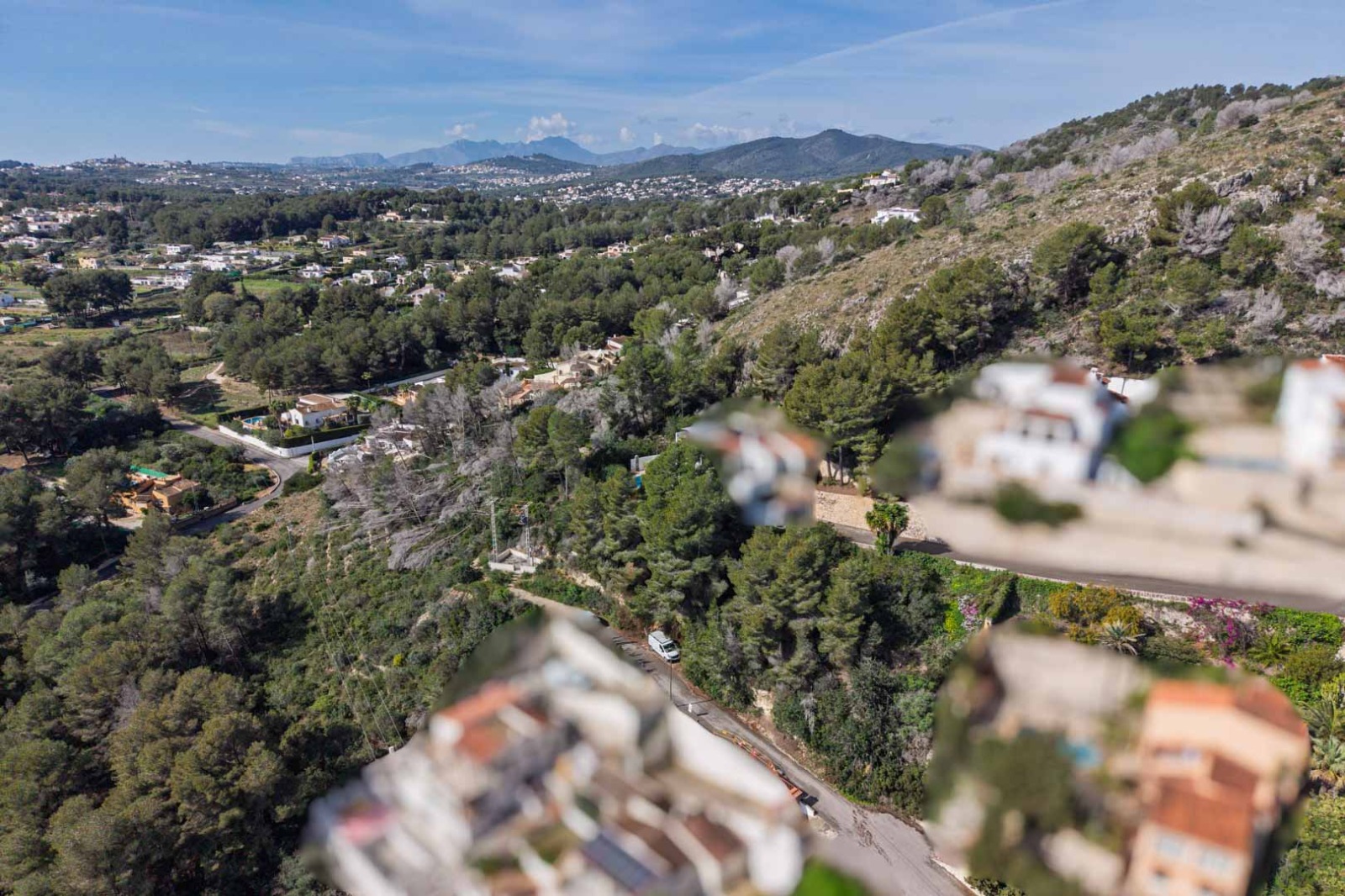 Panoramisch luchtaanzicht van de urbanisatie Sol de Este, met dichte dennenbossen, omliggende heuvels en verre bergketens onder een heldere blauwe lucht.