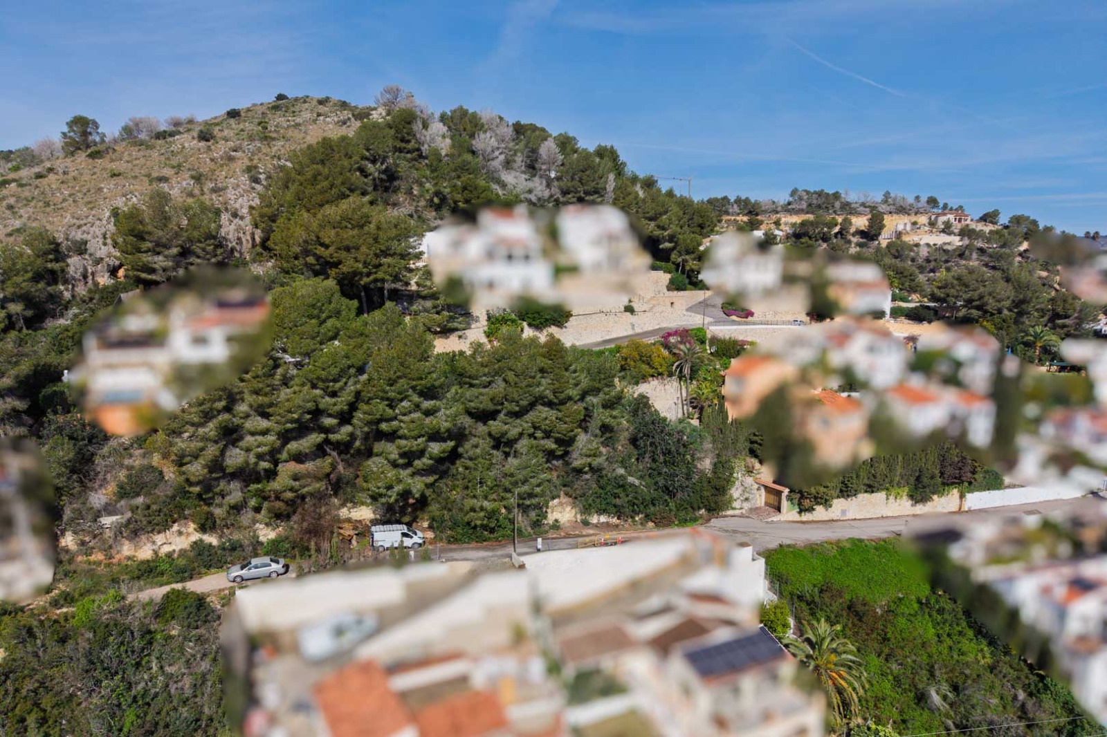 Verhoogd zicht op de beboste heuvel in Sol de Este, met mediterrane villa's tussen de dennenbomen en geasfalteerde toegangswegen met stenen muren.