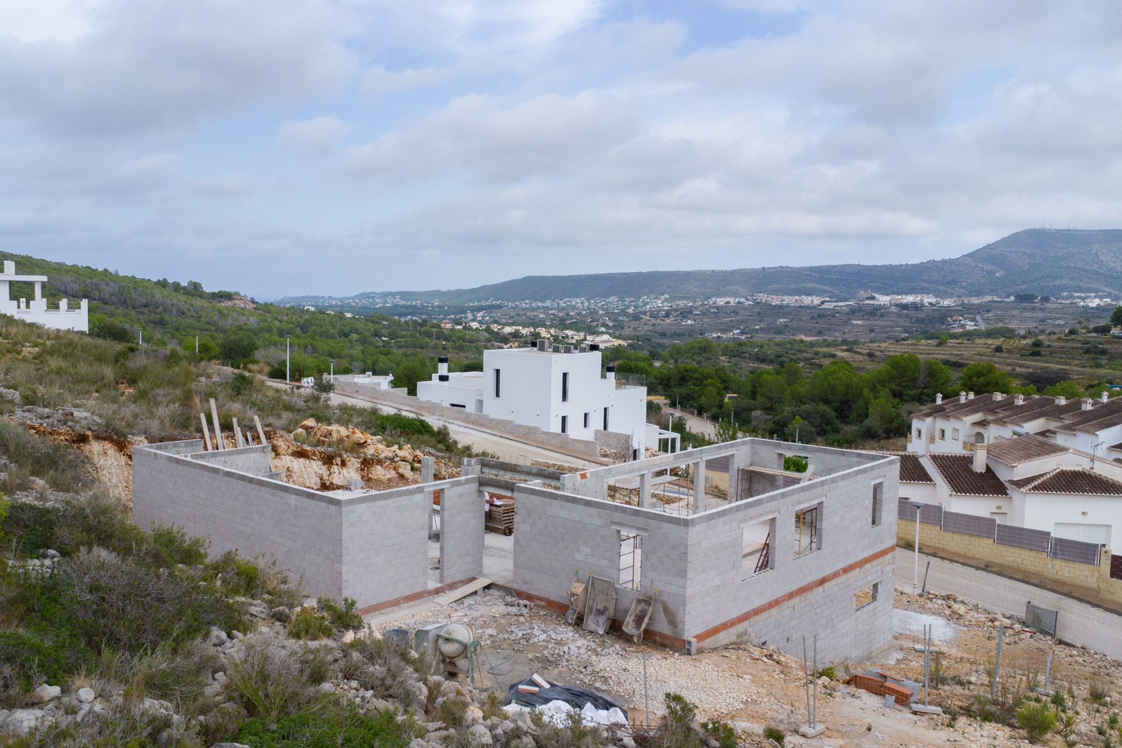 Bouwfase van een moderne villa in Pedreguer, met de betonblokkenstructuur en panoramisch uitzicht over de vallei en de omliggende bergen.