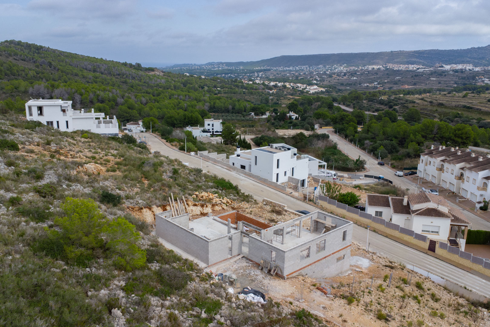 Luchtfoto van de villa in aanbouw in Pedreguer, met de betonstructuur op een helling en een panoramisch uitzicht over de vallei en omliggende natuur.