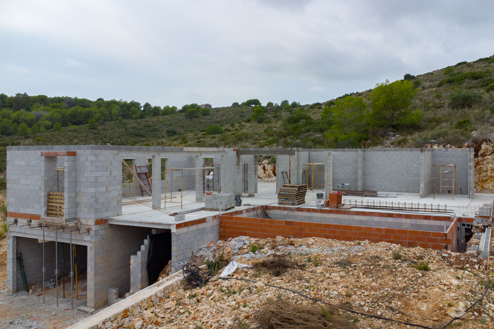 Moderne villa in aanbouw in Pedreguer met betonnen muren, een zwembadstructuur en een verhoogde ligging tegen de heuvel.