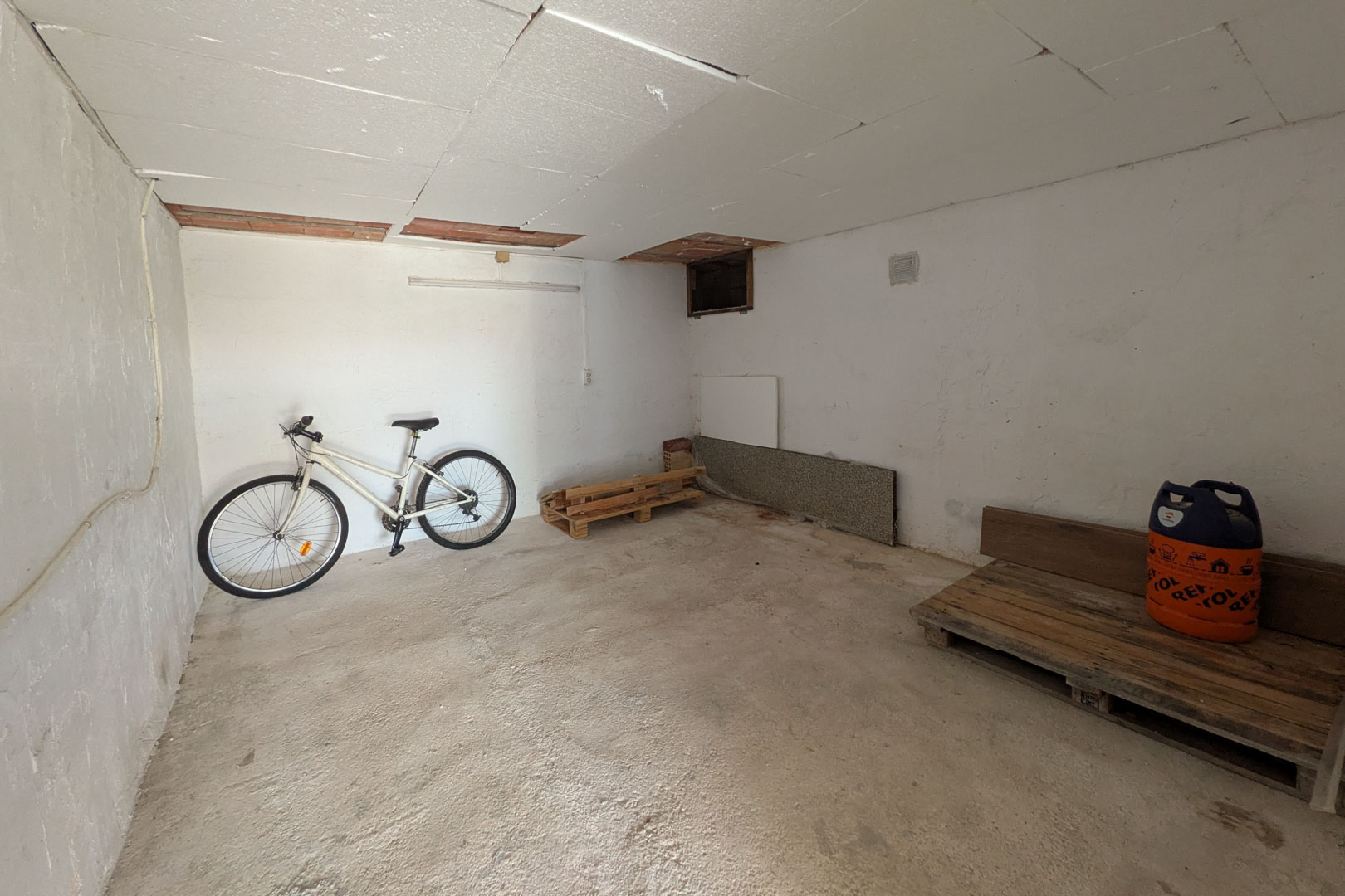 Onafhankelijke berging met paneelplafonds, een cementvloer en veelzijdige ruimte voor de opslag van fietsen of goederen.