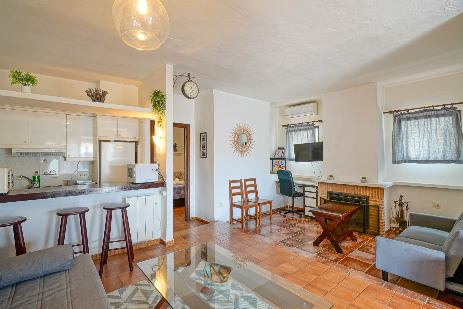 Open woonkamer met een bakstenen open haard, terracotta vloer en een halfopen keuken met een houten ontbijtbar.