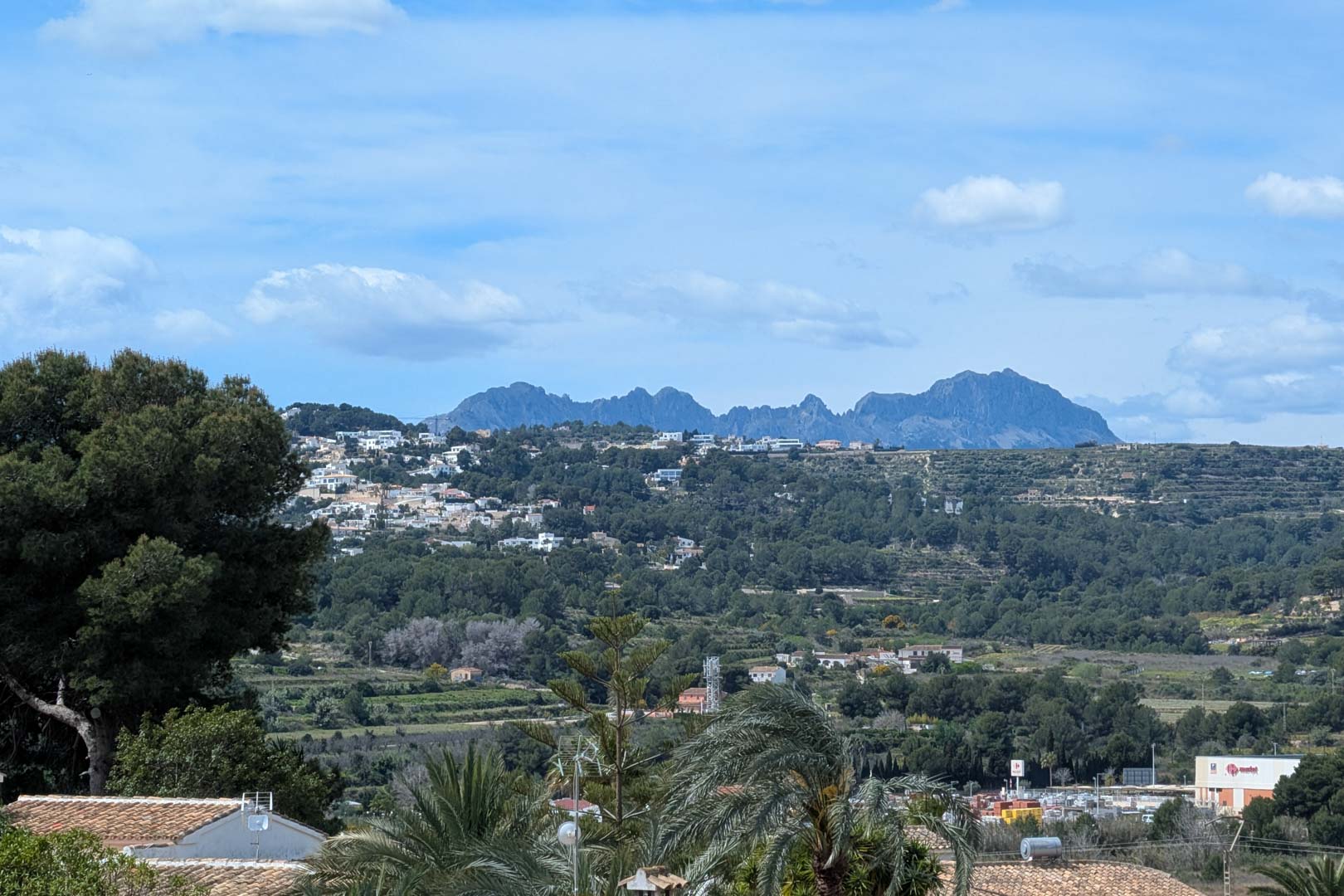 Panoramisch uitzicht vanaf het terras op de vallei en de bergen, met mediterrane vegetatie en het residentiële landschap van Moraira onder een heldere hemel.