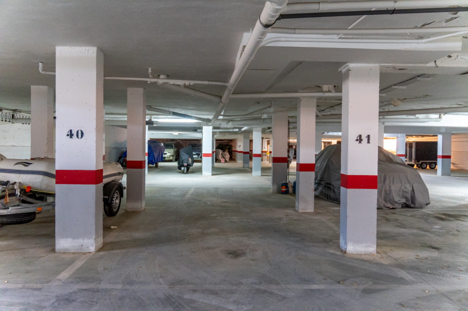 Ondergrondse parkeergarage met genummerde kolommen en afgedekte voertuigen.