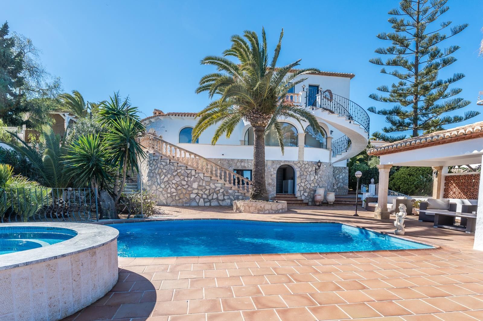 Buitenaanzicht van de villa met zwembad, ronde jacuzzi en natuurstenen gevel. Met een opvallende wenteltrap en mediterrane tuin met palmbomen en terrassen.