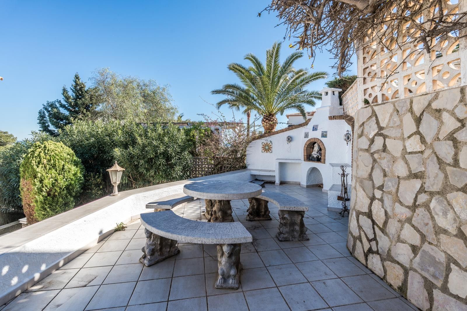 Buitenterras met een gebeeldhouwde stenen tafelset, een geïntegreerde gemetselde barbecue en muren bekleed met natuursteen in een mediterrane omgeving.