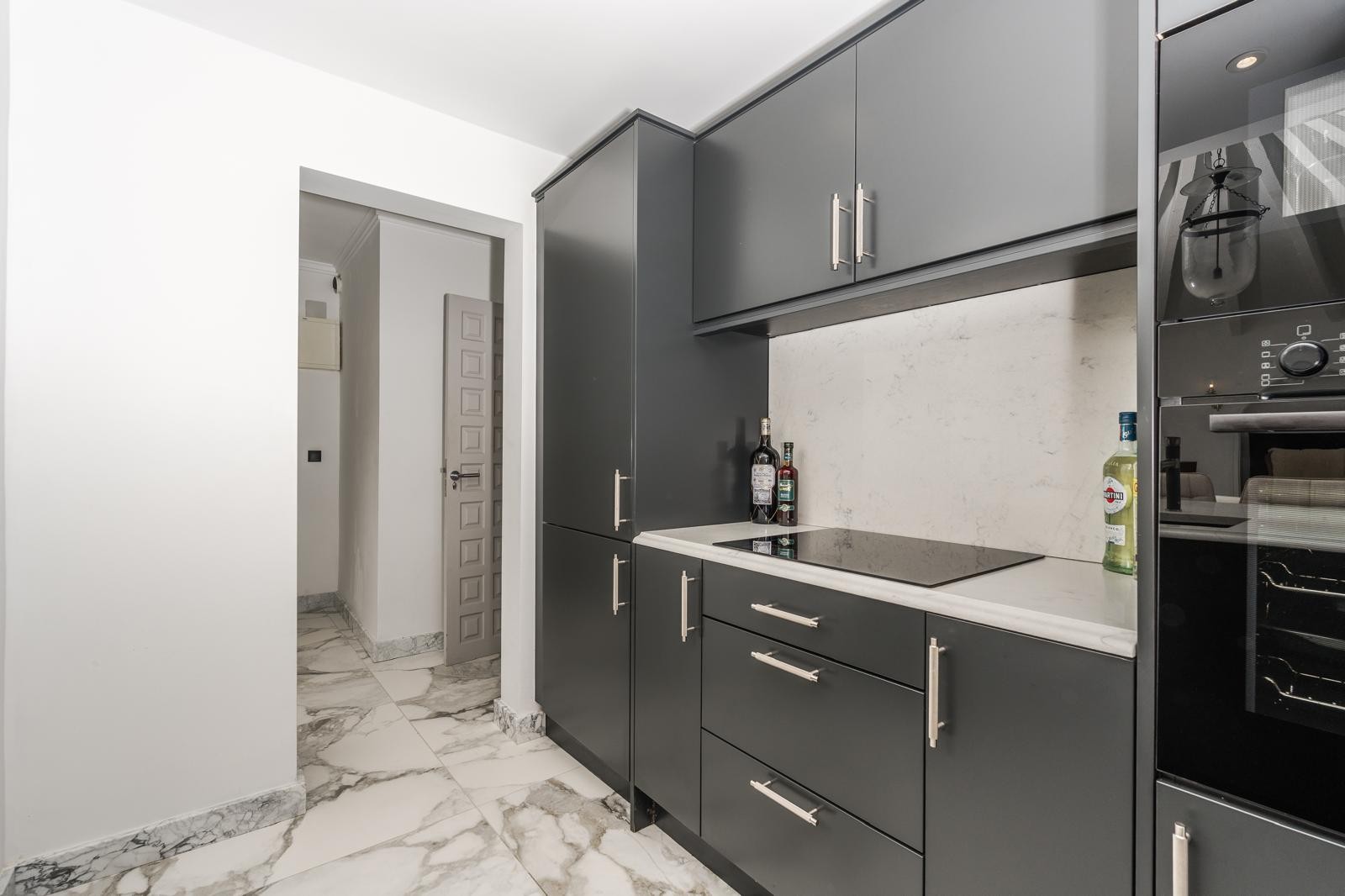 Eigentijdse keuken met donkergrijze kasten, wit marmeren aanrechtblad en inductiekookplaat op een elegante marmeren vloer met aders.