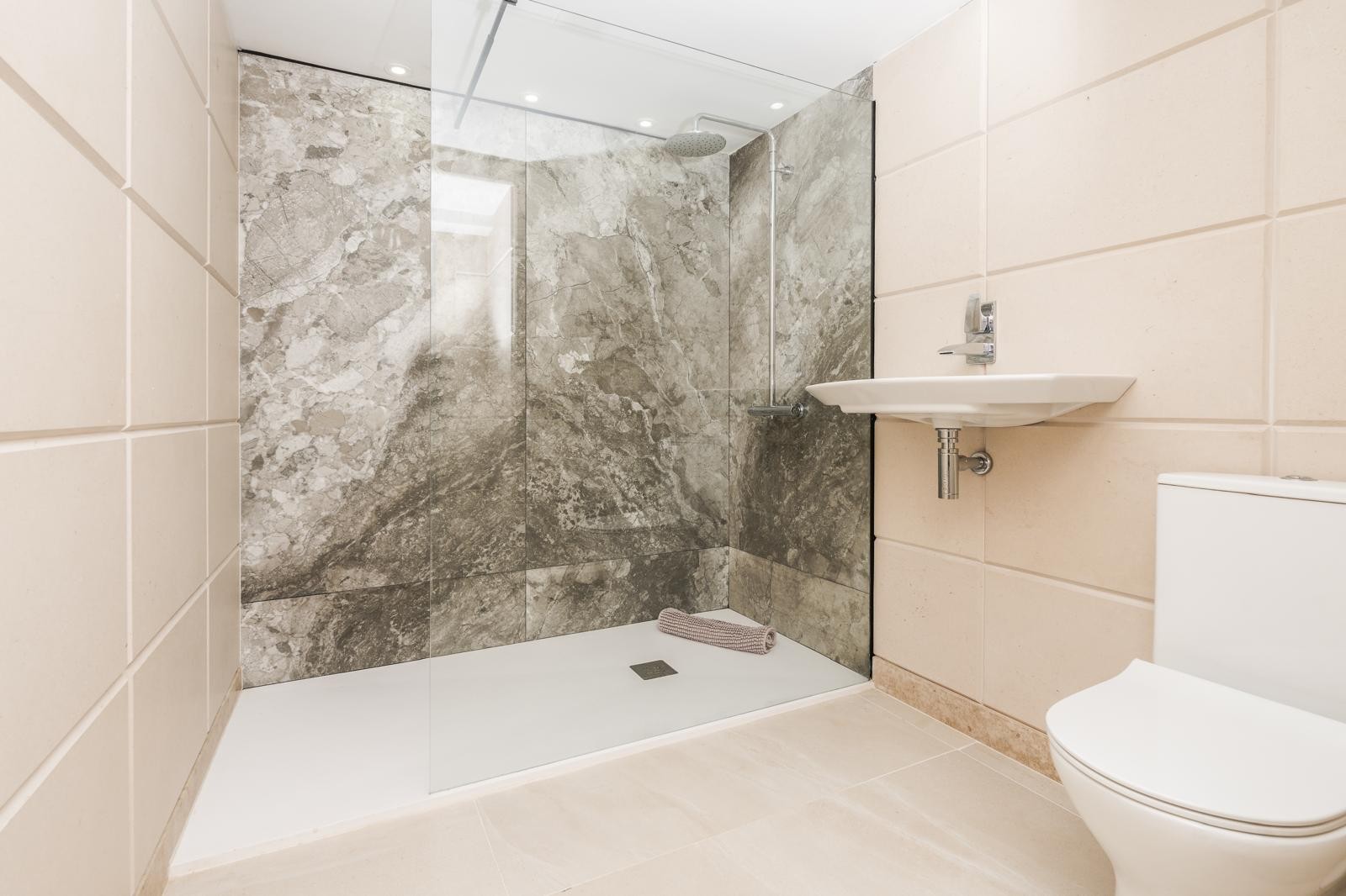 Moderne badkamer voorzien van een inloopdouche met grijs marmeren wanden, een glazen douchescherm en strak wit sanitair.