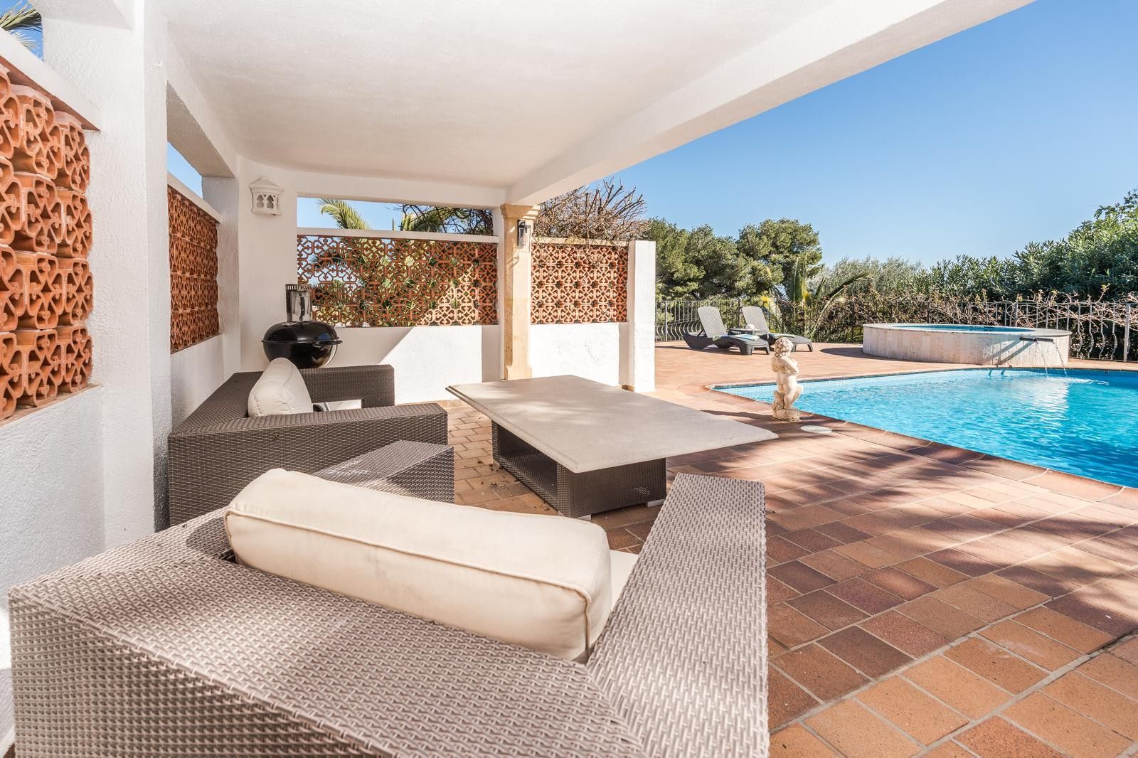 Overdekt terras met rotan loungemeubels en terracotta decoratieve wanden, grenzend aan het zwembad en de ronde buitenjacuzzi.