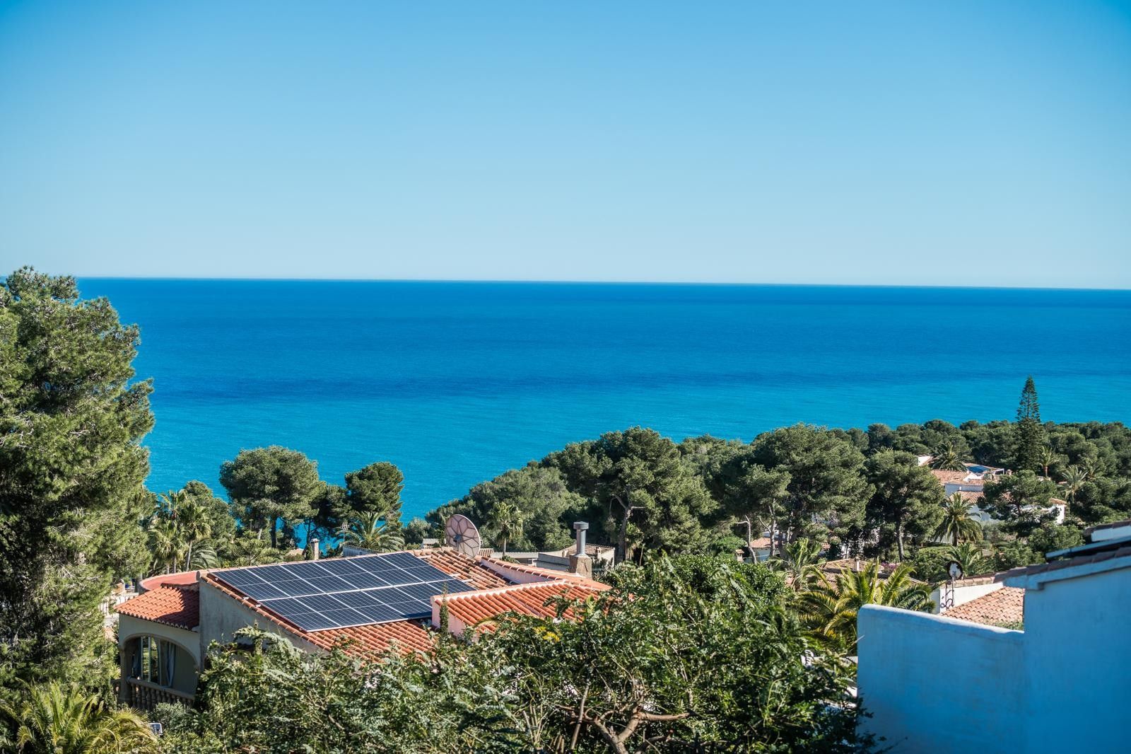 Panoramisch uitzicht op de Middellandse Zee in Balcón al Mar, uitkijkend over pijnbomen en daken met zonnepanelen onder een helderblauwe hemel.