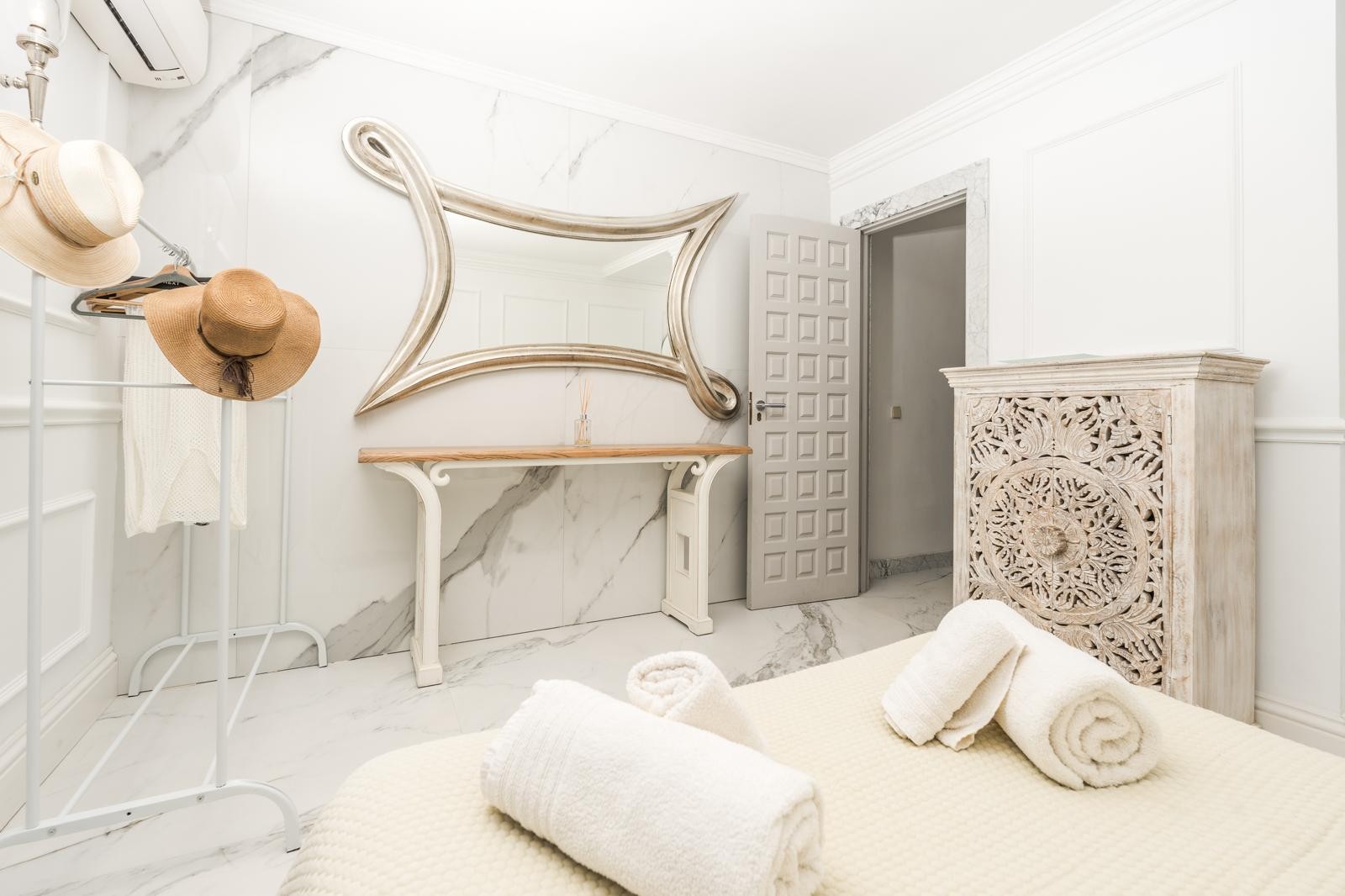 Slaapkamer met marmeren wanden en vloeren, een sierlijke zilveren spiegel en een handgesneden decoratieve houten kast.