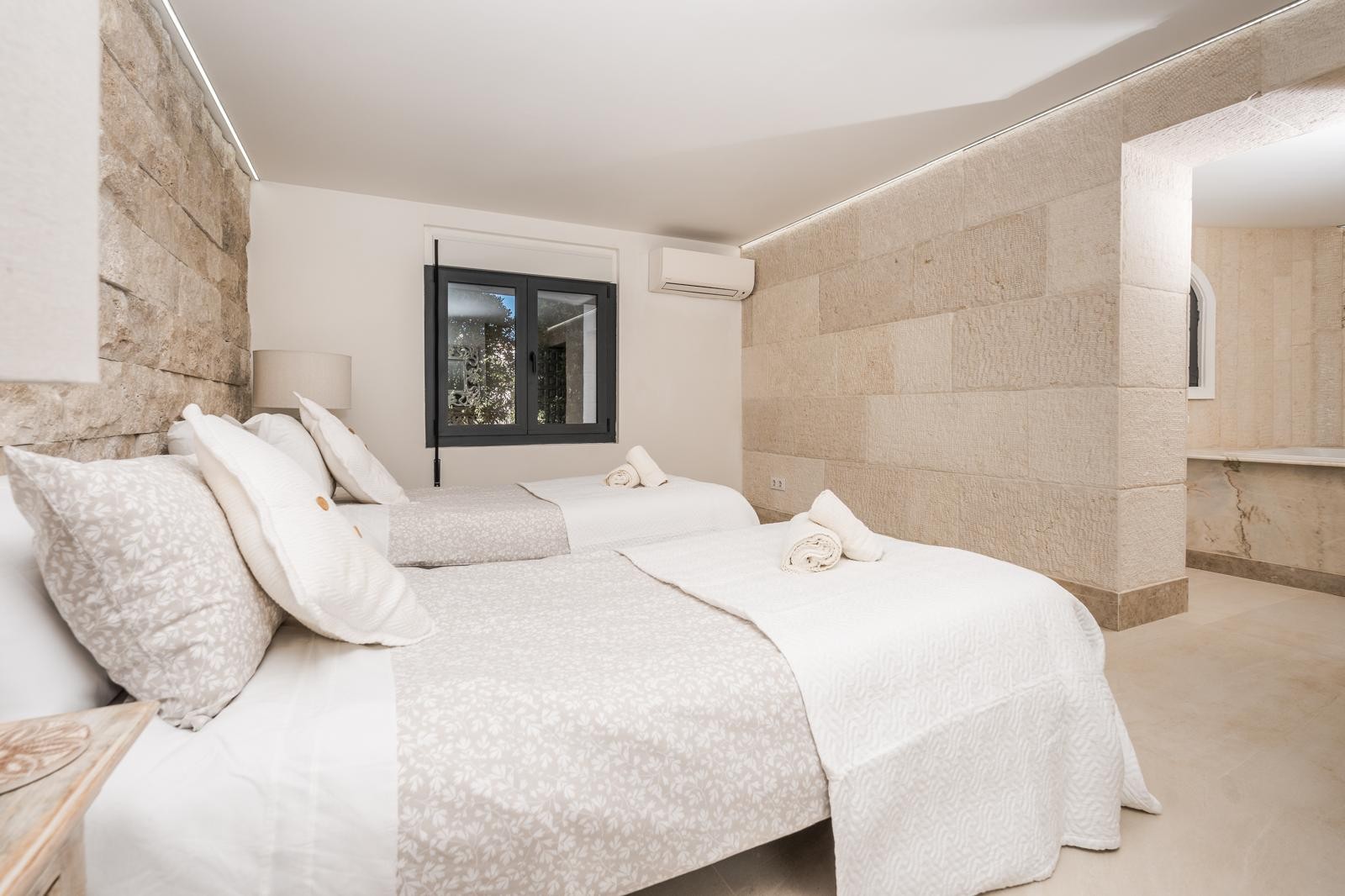 Slaapkamer met natuurstenen muren, indirecte LED-verlichting en twee eenpersoonsbedden. Voorzien van airconditioning en toegang tot een badkamer met marmeren details.
