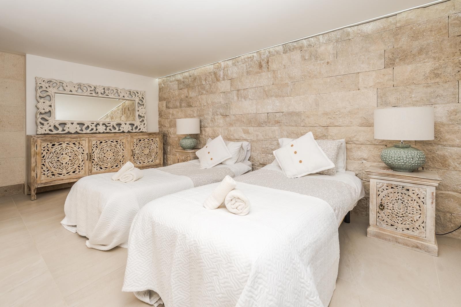 Slaapkamer met twee eenpersoonsbedden, een wand van natuursteen en handgesneden houten meubels die zorgen voor een warme, mediterrane sfeer.