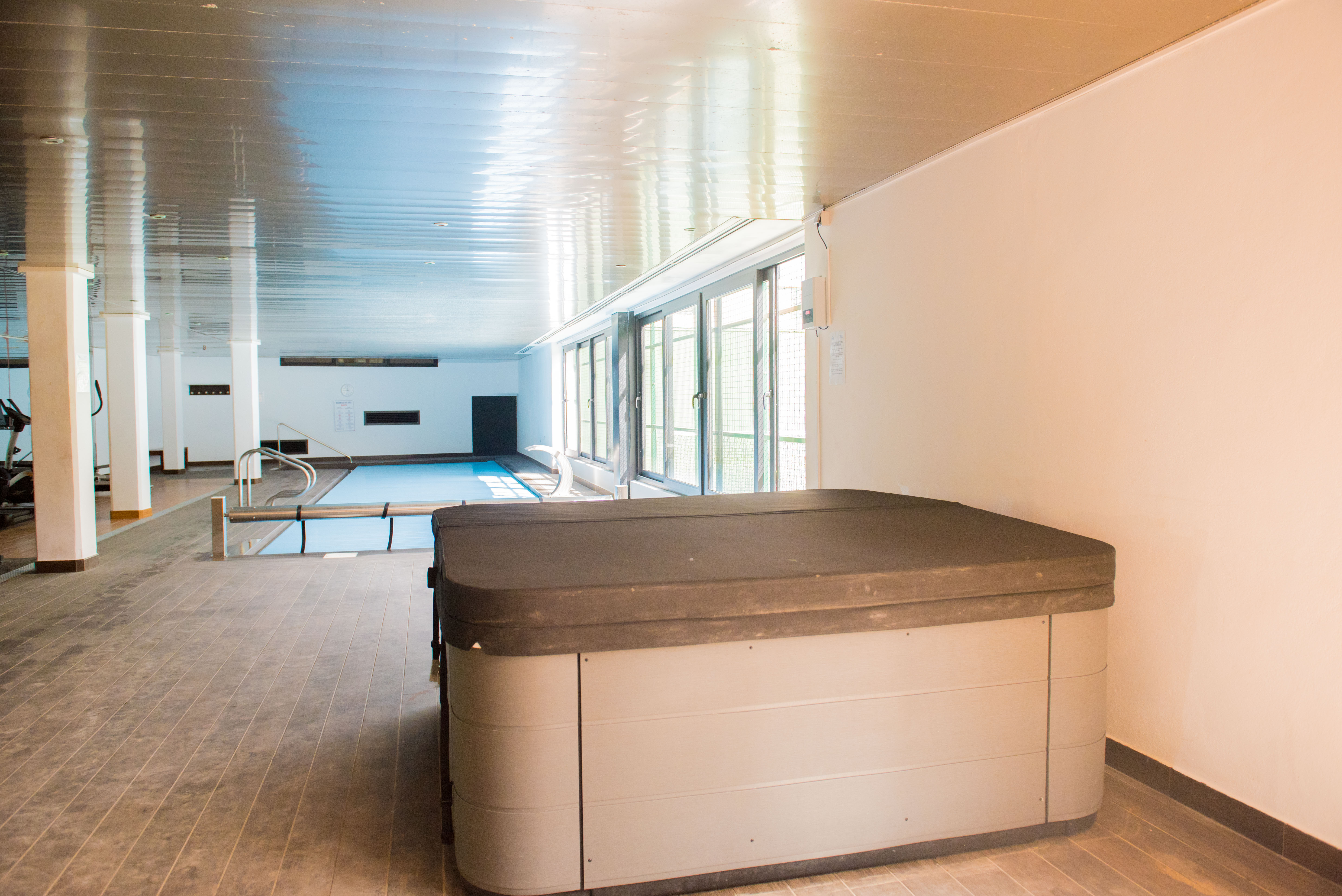 Binnenzwembad en wellnessruimte met een afgedekte jacuzzi en fitnessgedeelte, voorzien van grote ramen voor natuurlijk licht.