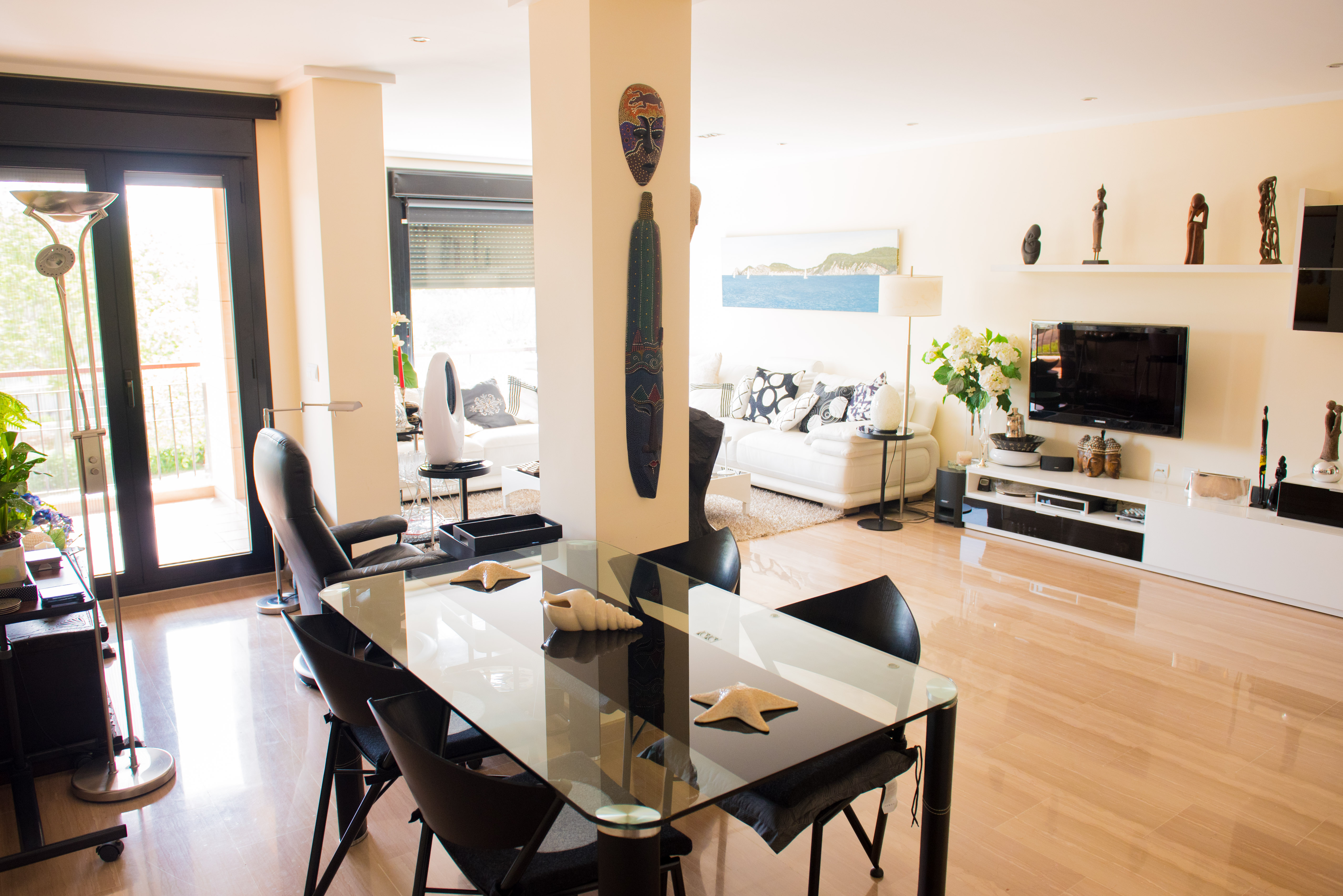 Lichte woon- en eetkamer met gepolijste marmeren vloer, glazen eettafel en toegang tot het balkon. Moderne inrichting met etnische accenten en veel natuurlijk licht.