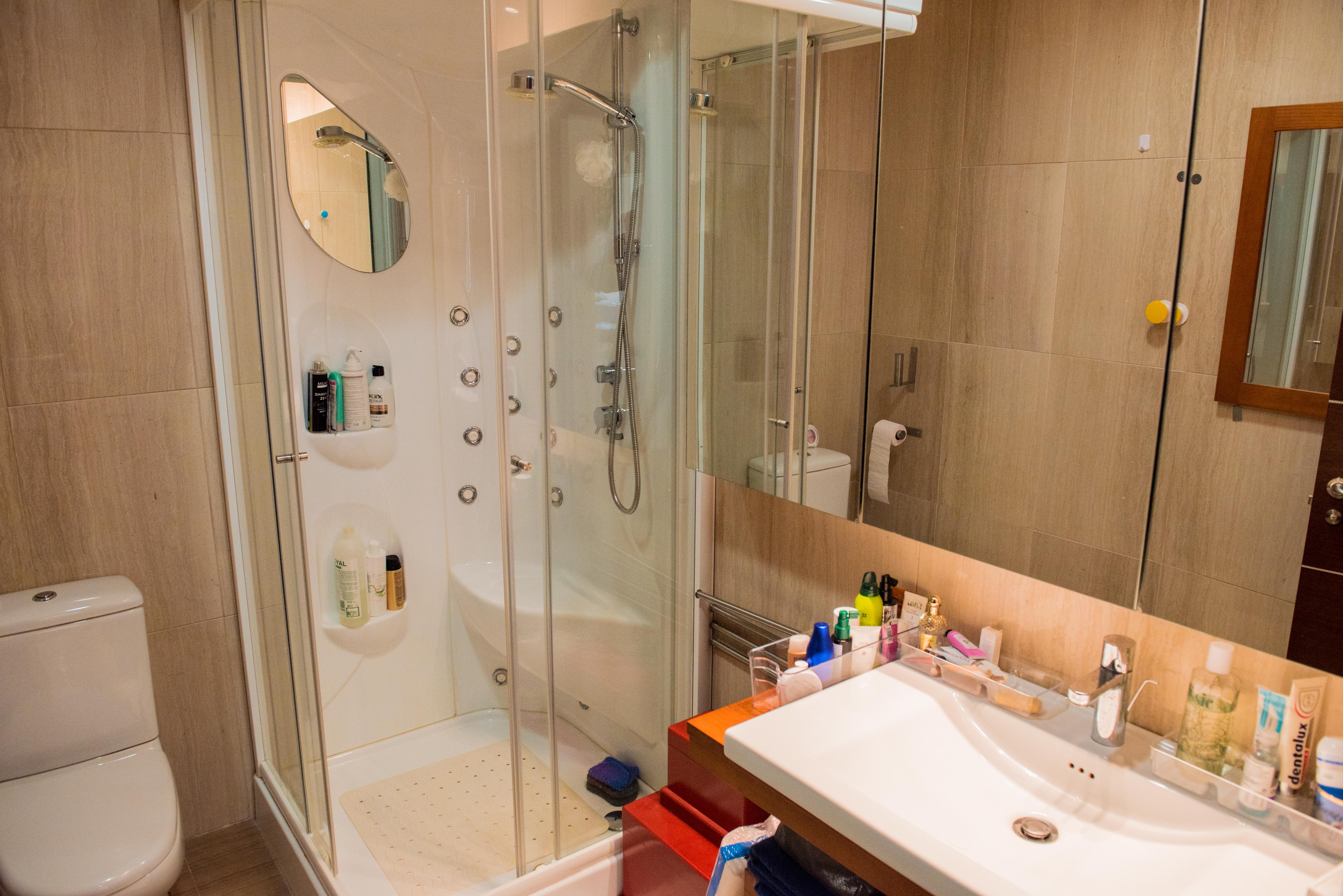 Moderne badkamer met hydromassage douchecabine, glazen deuren, witte design wastafel en wanden afgewerkt met neutrale porseleinen tegels.