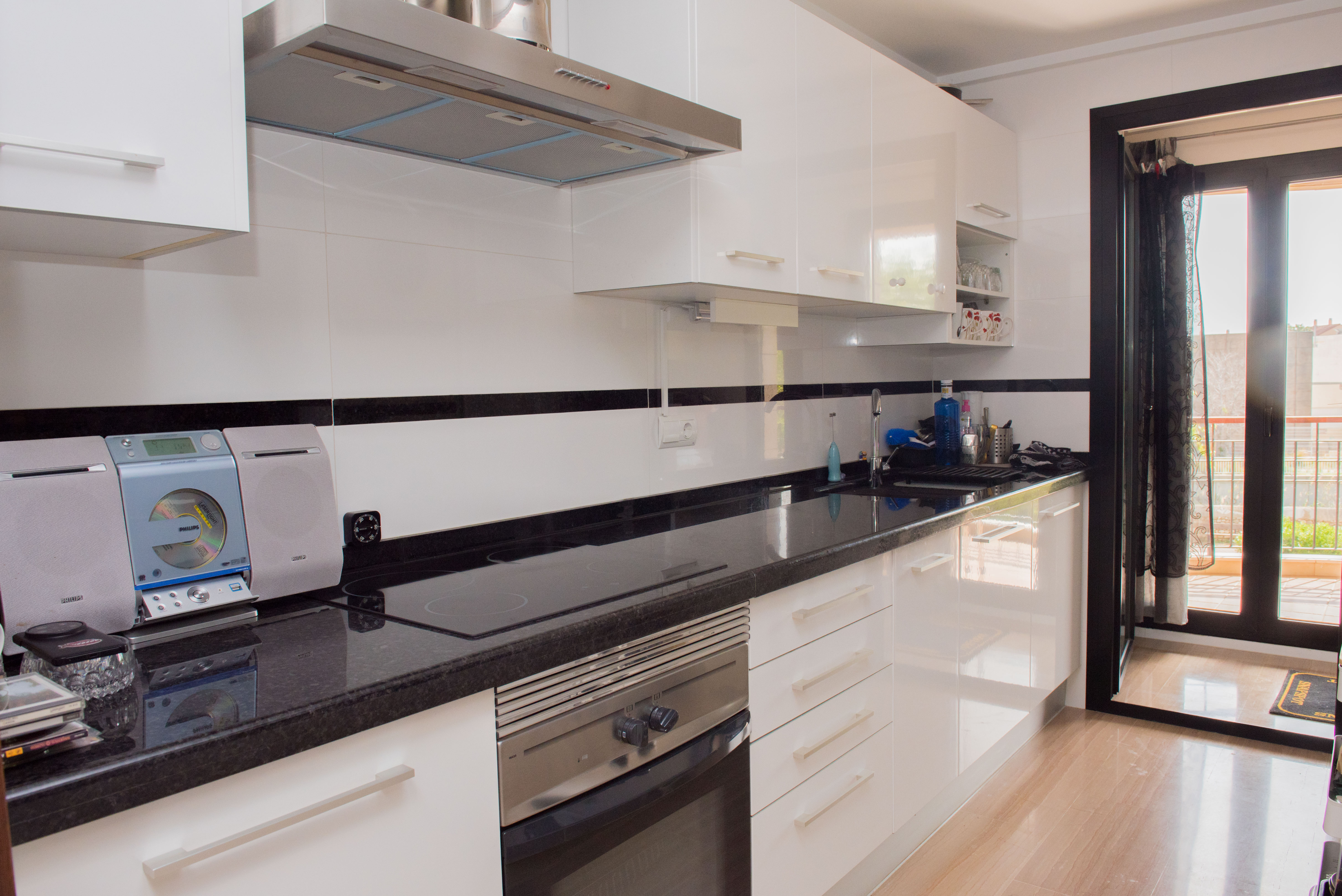 Moderne keuken met hoogglans witte kasten, zwart granieten aanrechtblad en rvs-apparatuur. Voorzien van directe toegang tot een buitenbalkon.