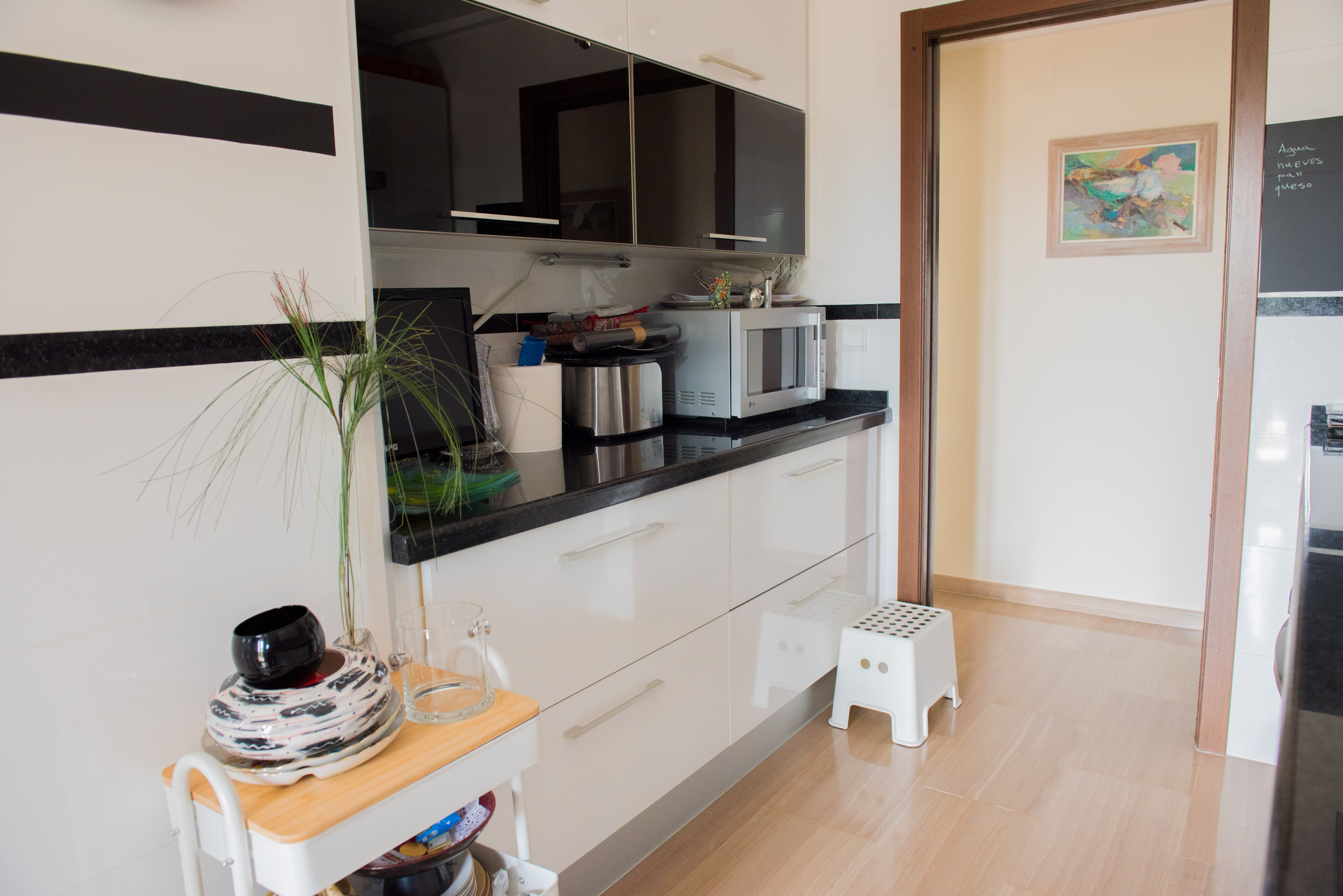 Moderne keuken met witte hoogglanskasten, zwarte glazen bovenkasten en een donker granieten werkblad. Voorzien van een lichte houten vloer en strakke afwerking.