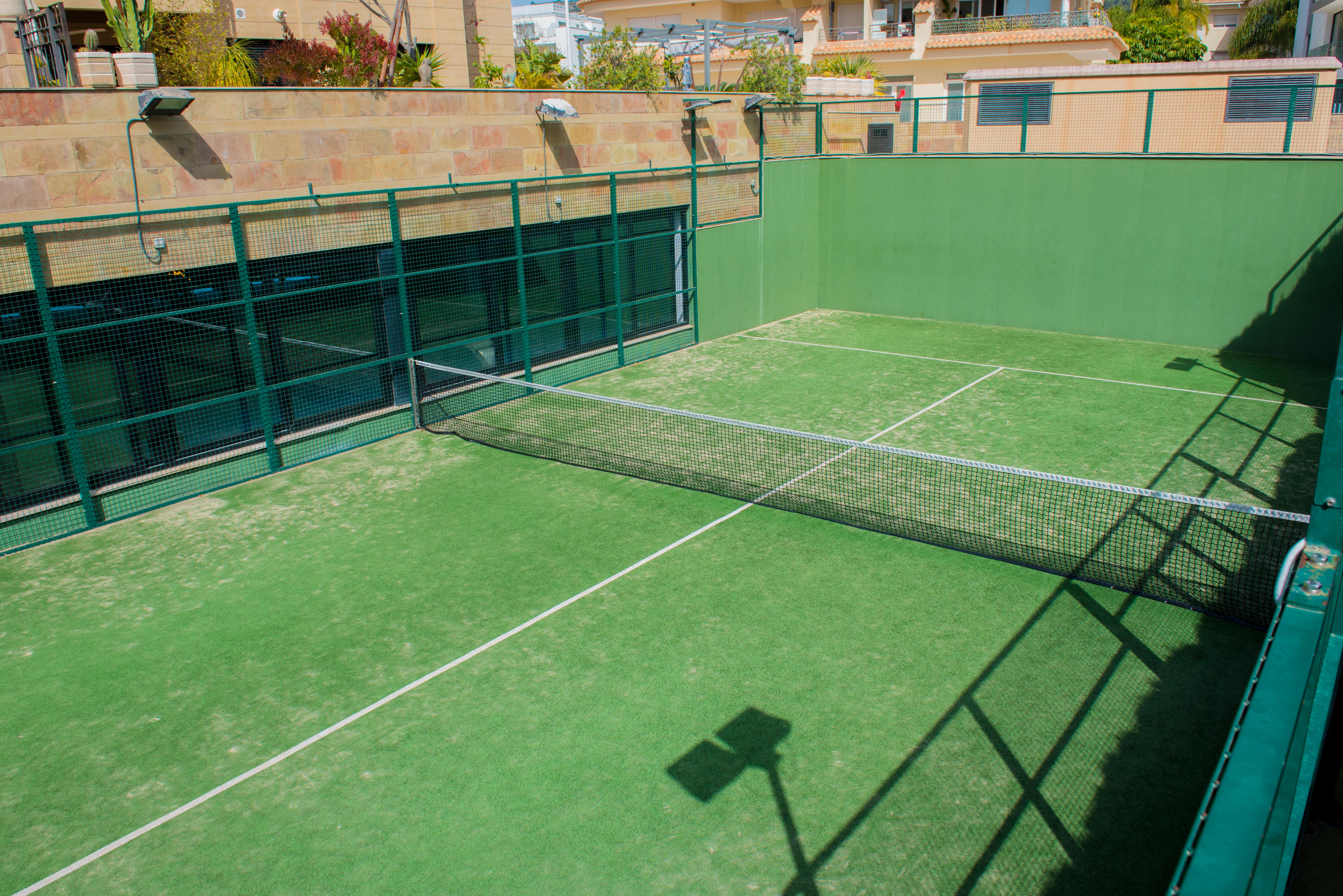 Privé padelbaan met groen kunstgras en metalen omheining, gelegen in de gemeenschappelijke ruimtes van het wooncomplex in Jávea.