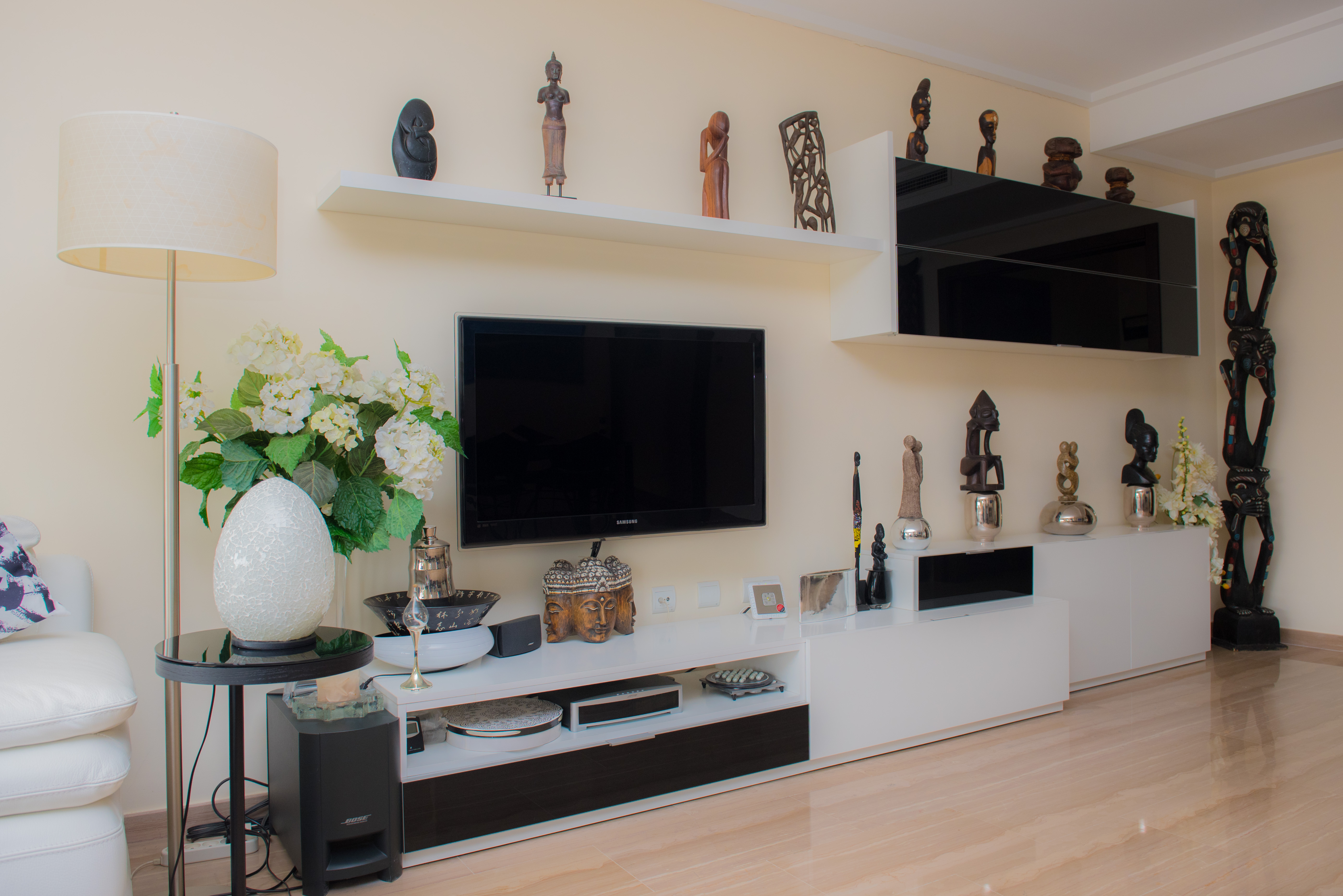Woonkamer met een modern zwart-wit tv-meubel, zwevende planken met etnische kunst en een gepolijste natuurstenen vloer.