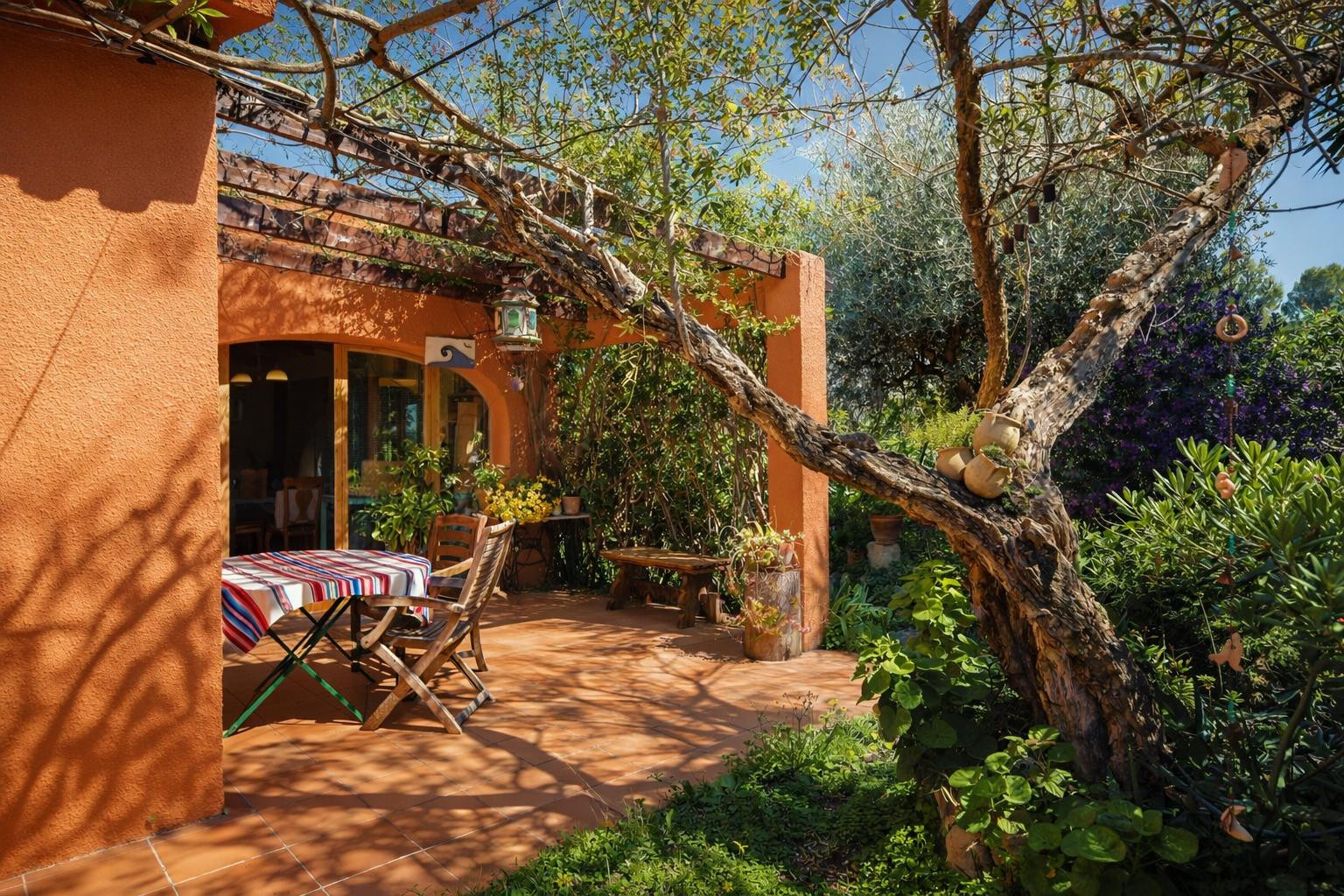 Buitenterras met terracotta tegels, een houten pergola en volgroeide beplanting die natuurlijke schaduw biedt boven de eethoek.