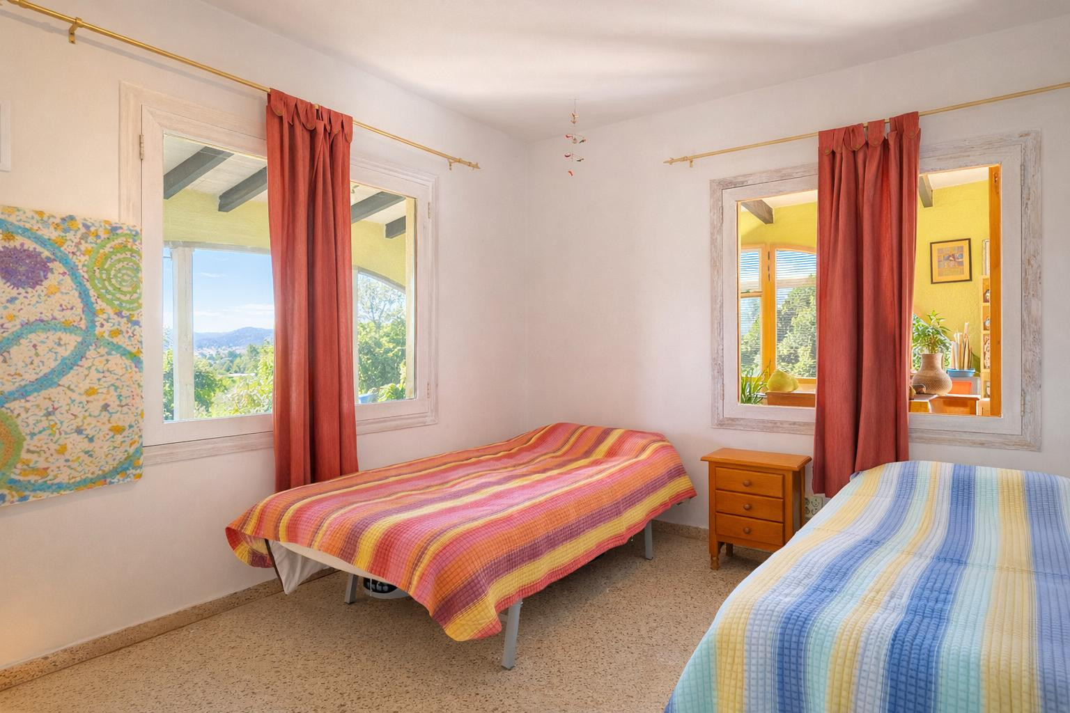 Lichte slaapkamer met twee eenpersoonsbedden, een houten nachtkastje en witte raamkozijnen met uitzicht op het landschap en de binnenruimtes.