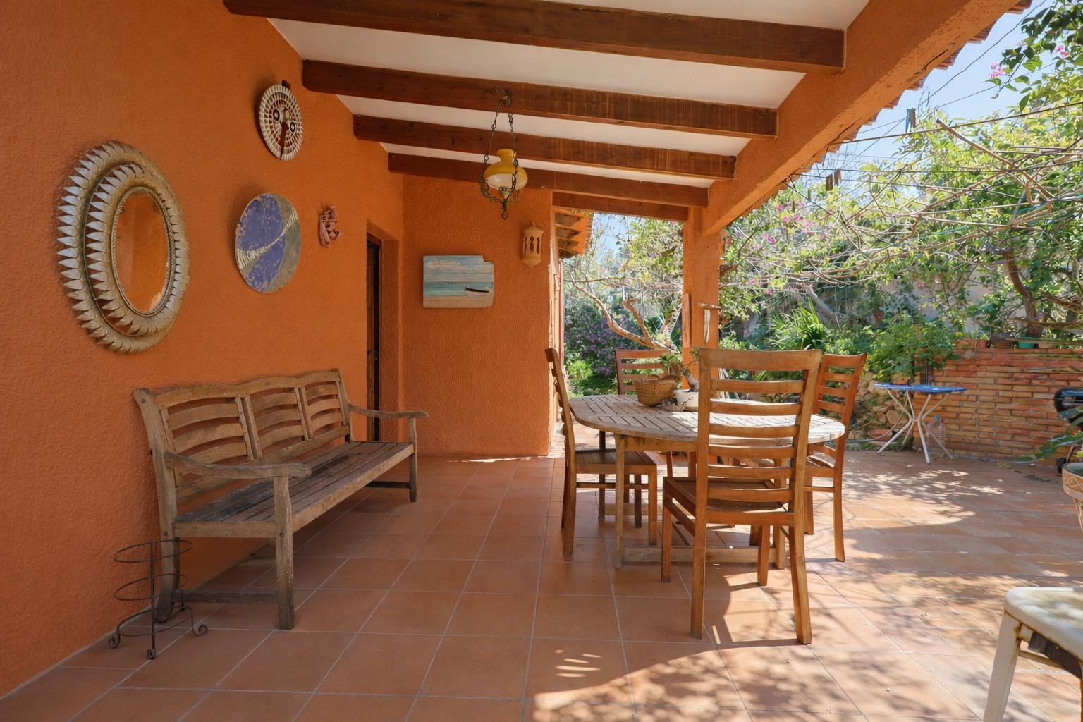 Overdekt terras met houten balkenplafond, terracotta vloertegels en een houten eethoek in een mediterrane sfeer.